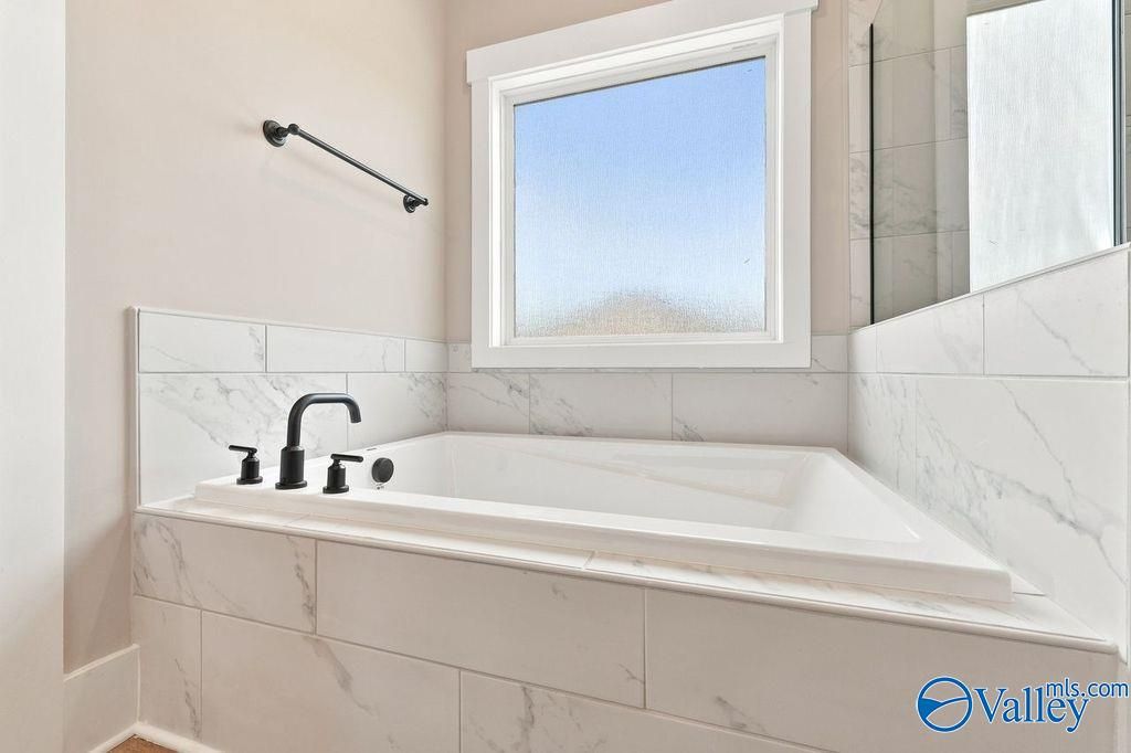 Modern soaking tub with matte black fixtures and marble-style tile surround in The Rockford home at Cain Park, Hartselle.