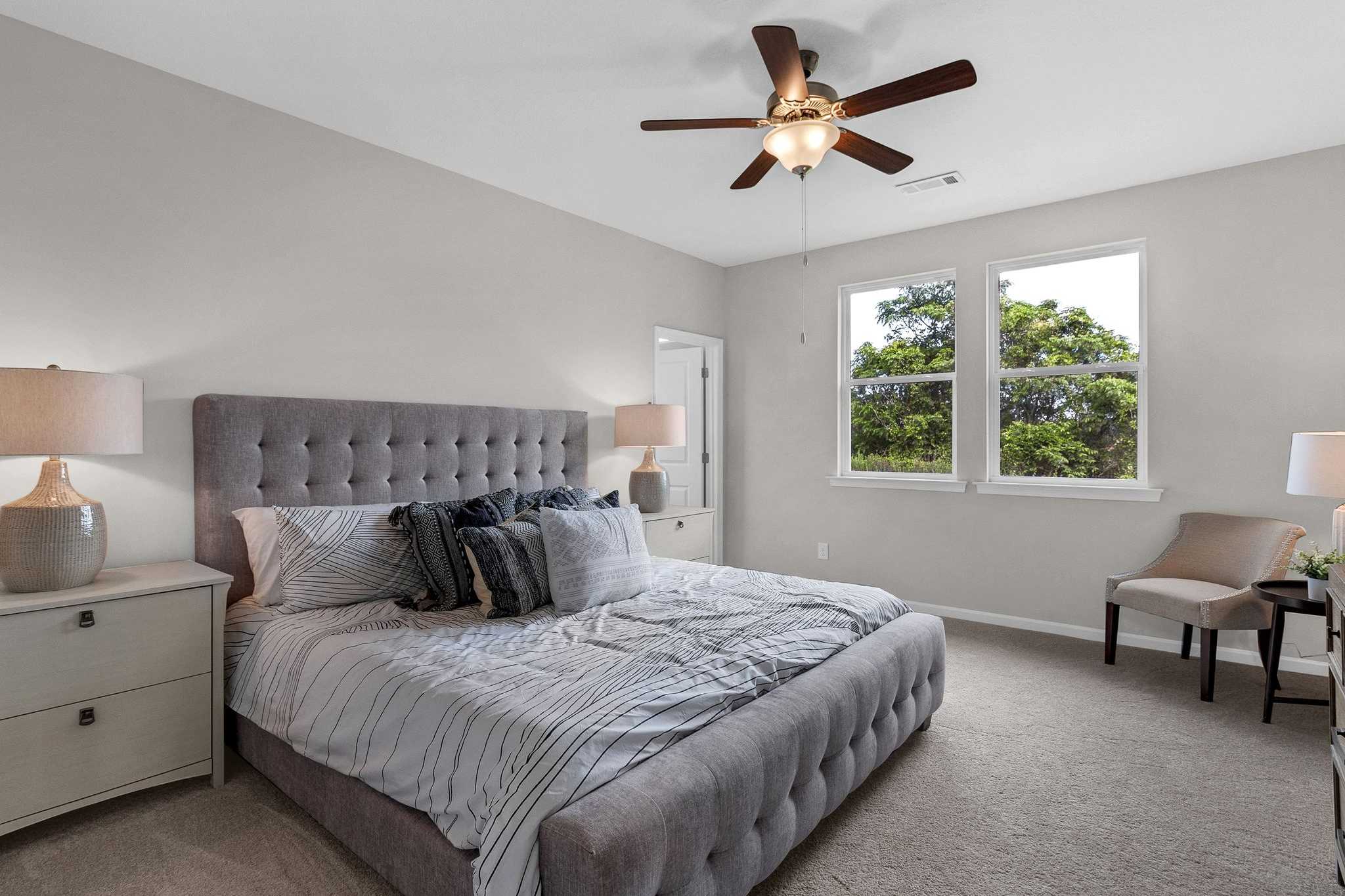 Spacious master bedroom in Ivy Glen Perry Georgia with tufted gray bed, ceiling fan, and large windows overlooking trees