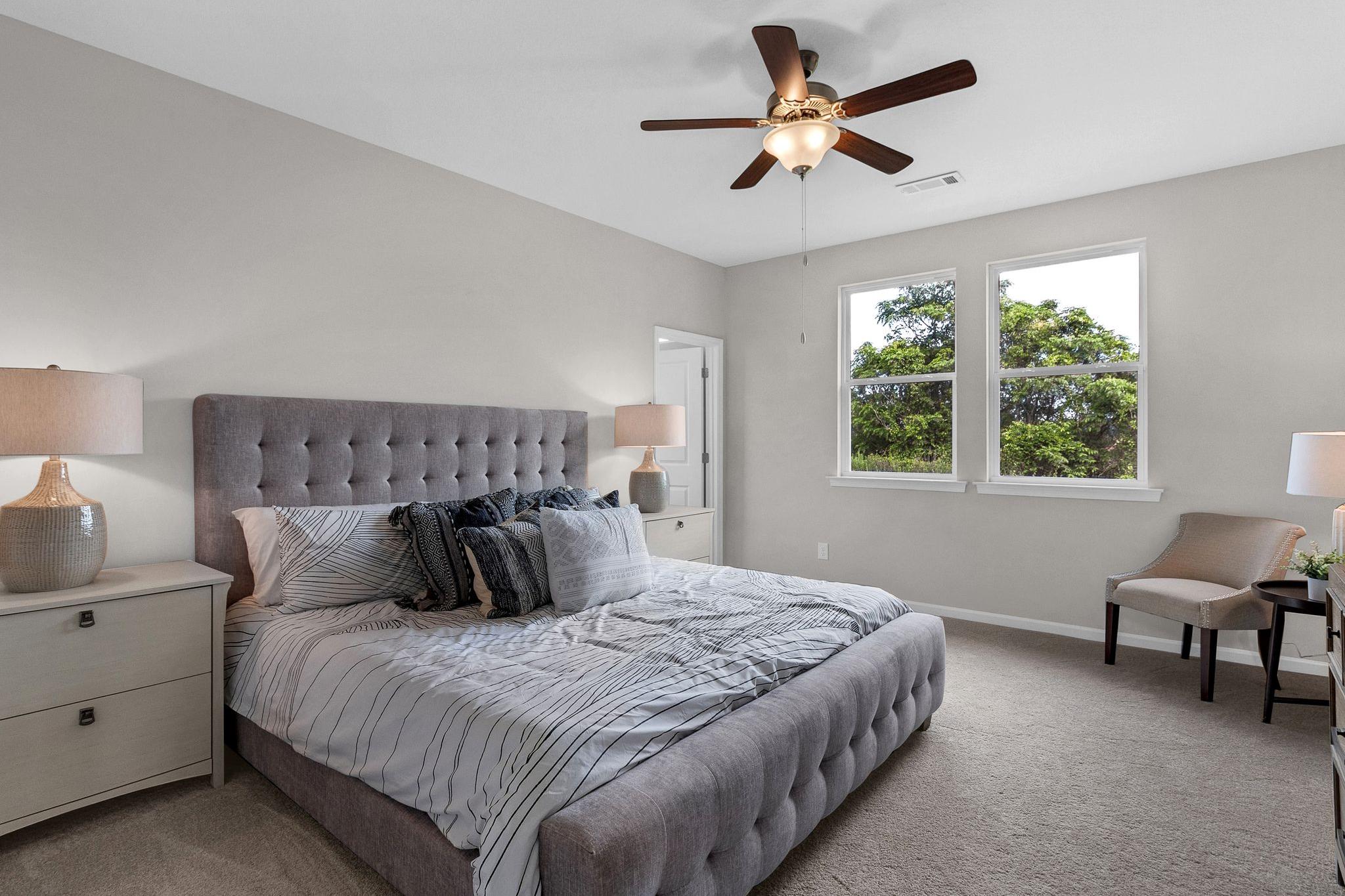 Spacious master bedroom in Ivy Glen Perry Georgia with tufted gray bed, ceiling fan, and large windows overlooking trees
