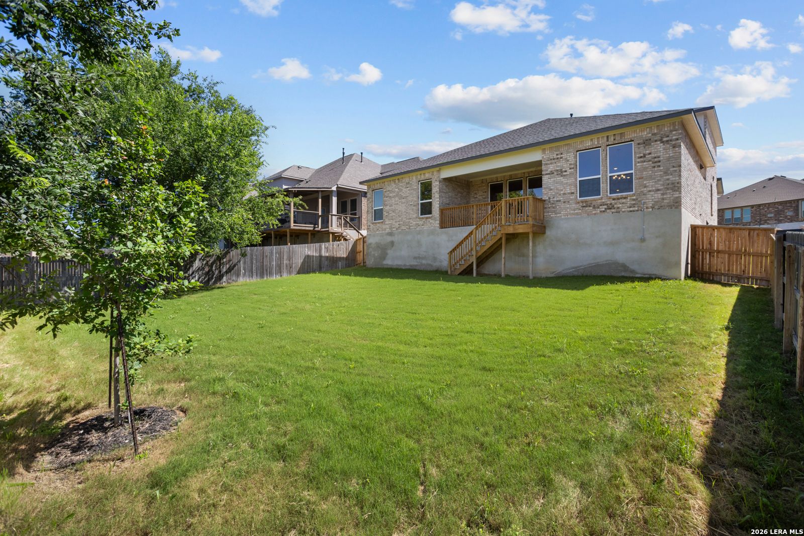 Large backyard with wooden deck, brick exterior, and lawn of The Jennings G floor plan by Davidson Homes in Ladera, TX.