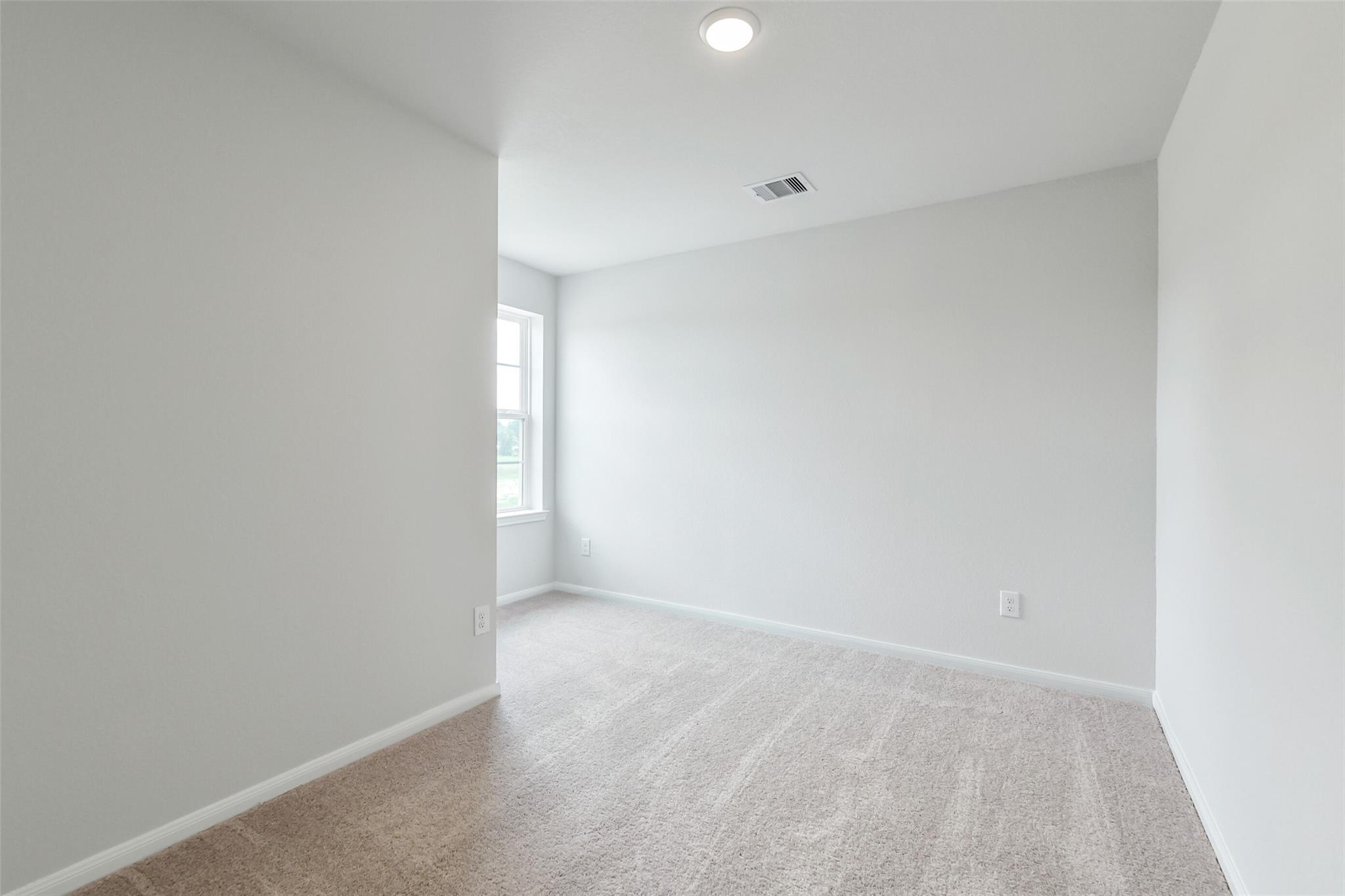 Bright secondary bedroom with neutral walls, beige carpet, large window, and recessed lighting in Davidson Homes Sabine E, Conroe TX