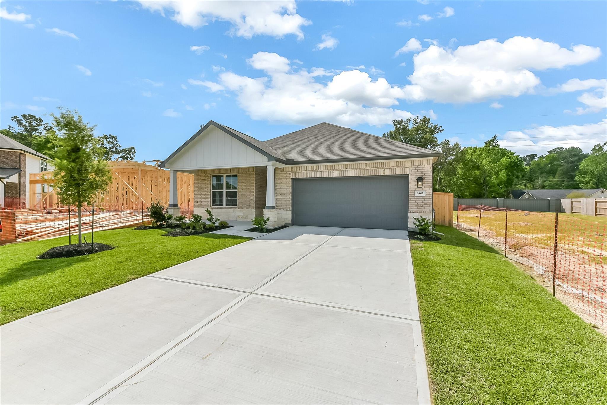 The Everett C 1-story brick home exterior with 2-car garage, concrete driveway, and green lawn in Sundance Cove, Crosby, Texas