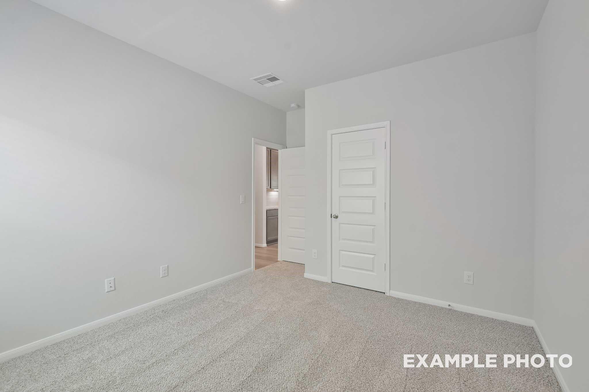 Empty secondary bedroom with neutral gray walls, beige carpet, and bathroom doorway in Davidson Homes The Frio F, Conroe, Texas