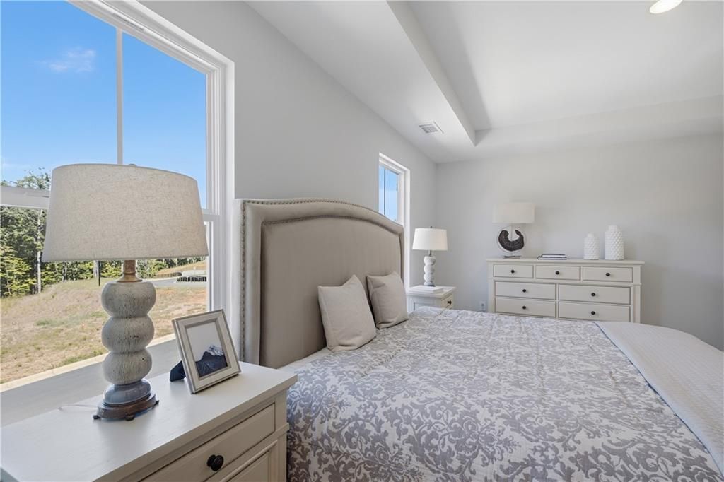 Bright primary bedroom with upholstered headboard, tray ceiling, and scenic views in Davidson Homes Hartwell C, The Bluffs, Canton GA