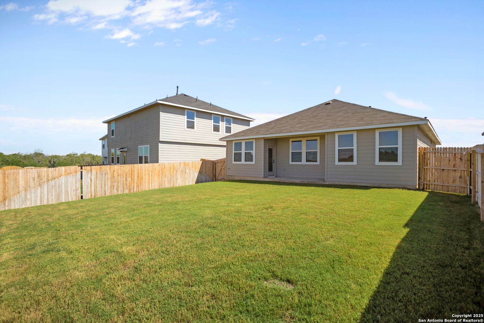 Single-story beige Asheville H home exterior with wooden privacy fence and lush green yard in Horizon Pointe, Converse, Texas