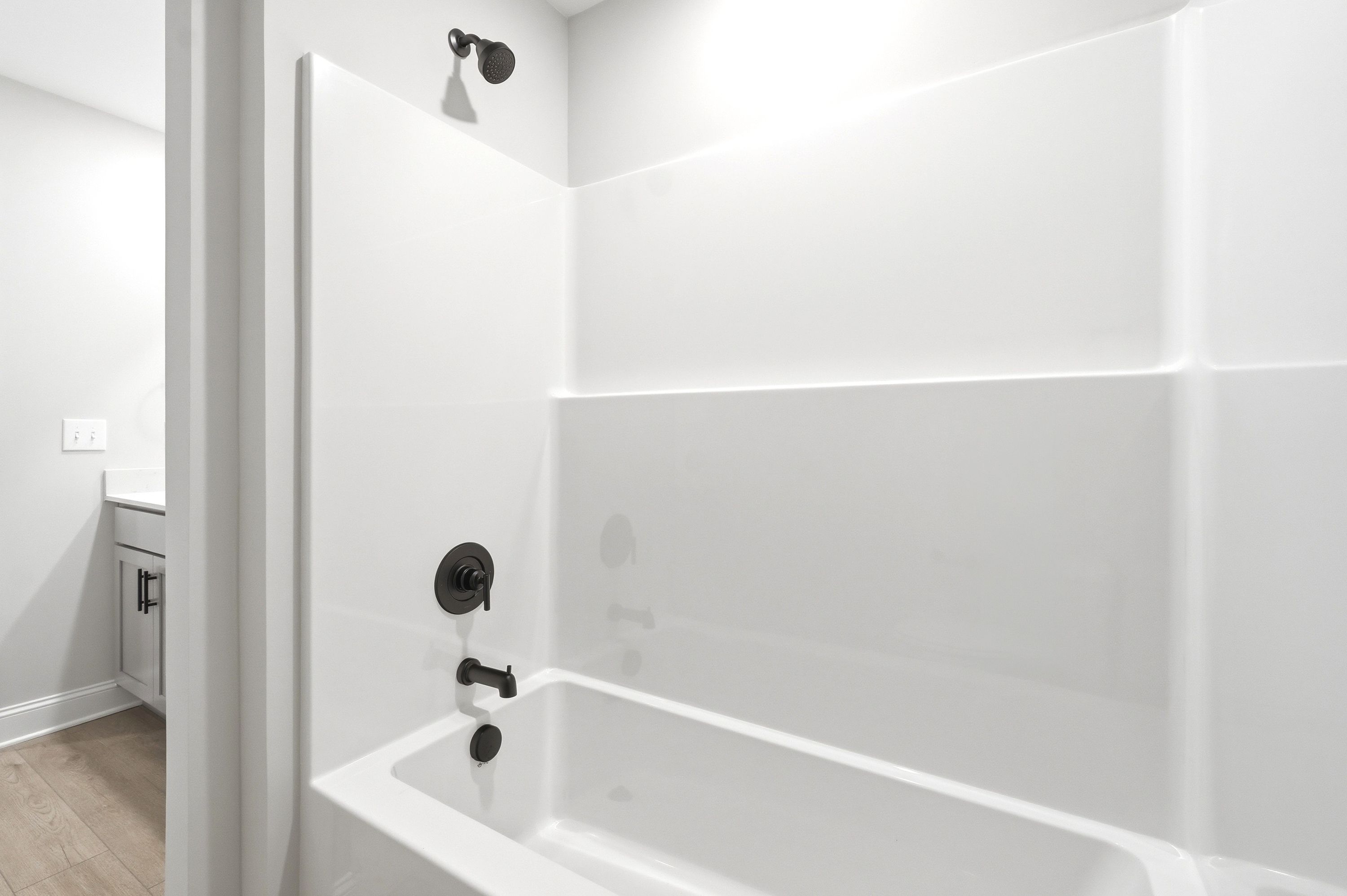 Modern bathroom in The Russell A featuring a white tub-shower combo with sleek matte black fixtures.
