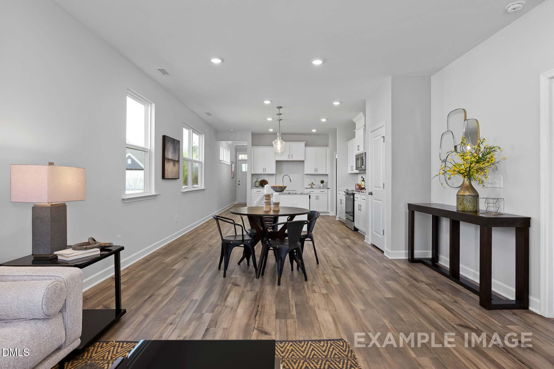Open-concept dining room with hardwood floors, black chairs, and adjacent white kitchen in Davidson Homes The Carter C, Lillington, NC