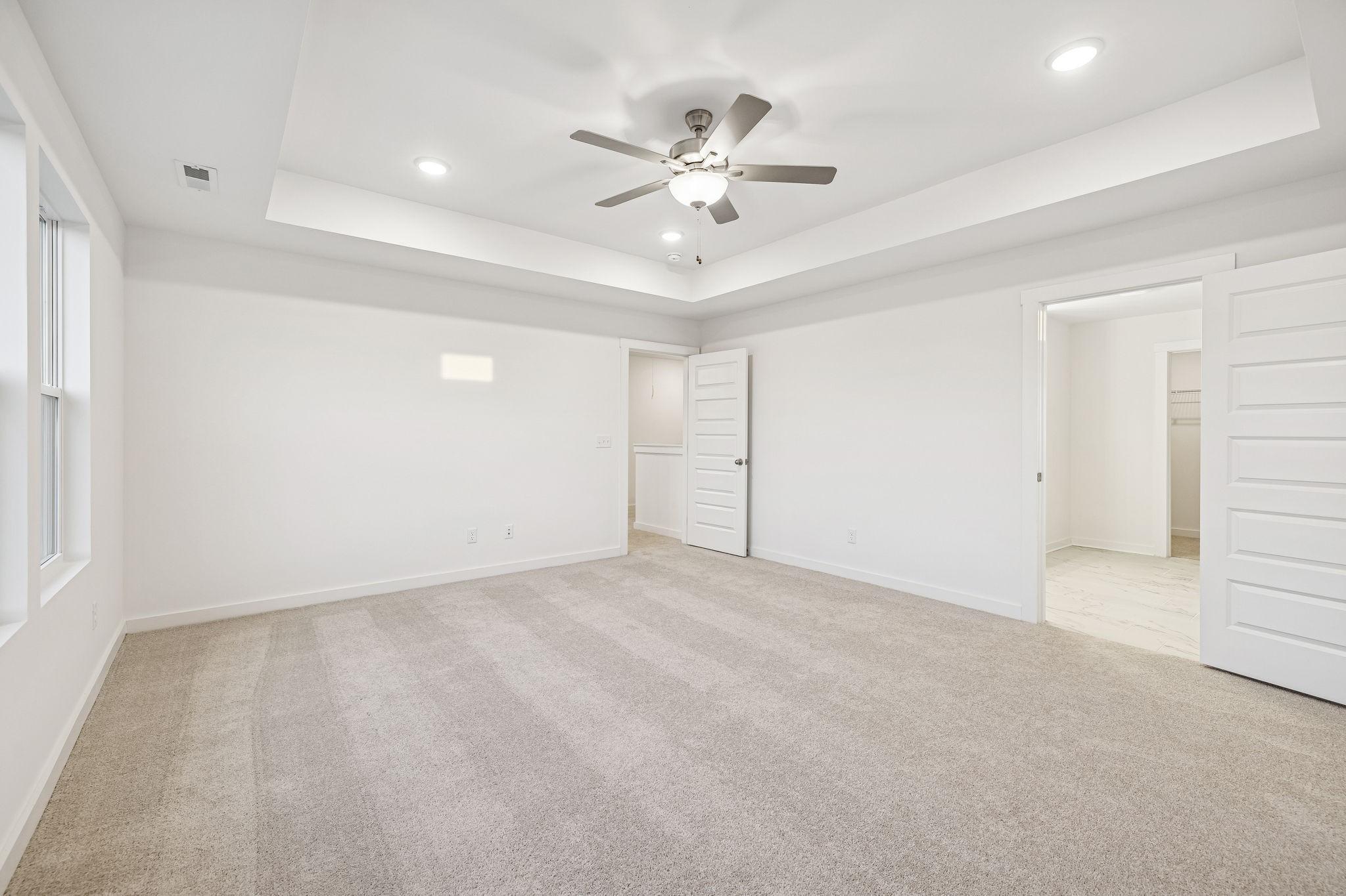 Spacious master bedroom with tray ceiling, ceiling fan, walk-in closet, and en-suite bath in Davidson Homes The Willow, Calista Farms