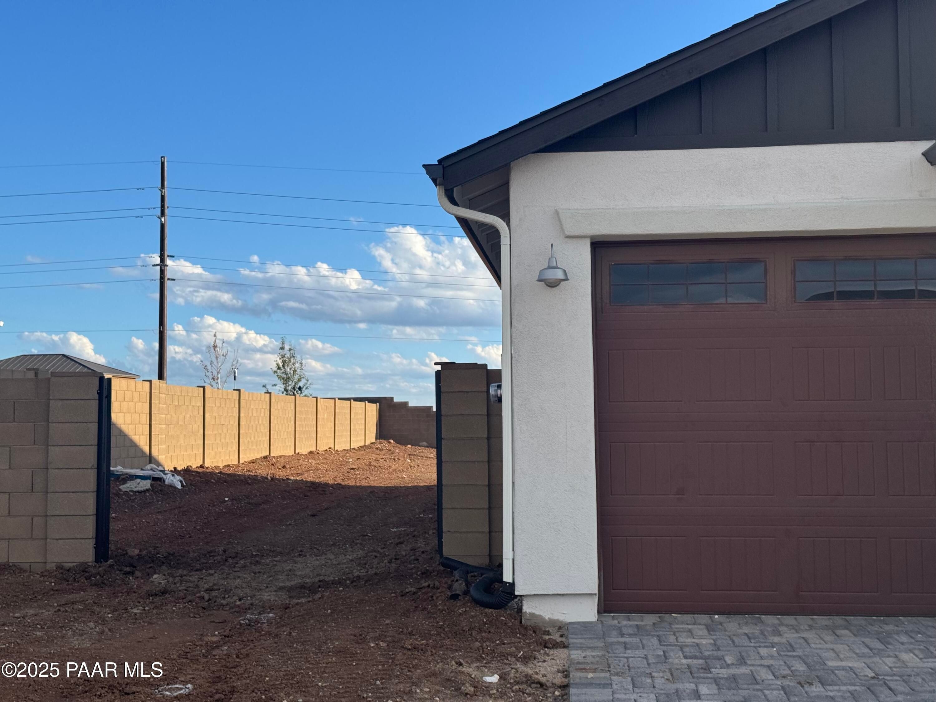 Modern 4-car garage with brown doors on white stucco Evermore Homes The Sunrise A in Morningstar, Prescott Valley, Arizona, block fence backdrop