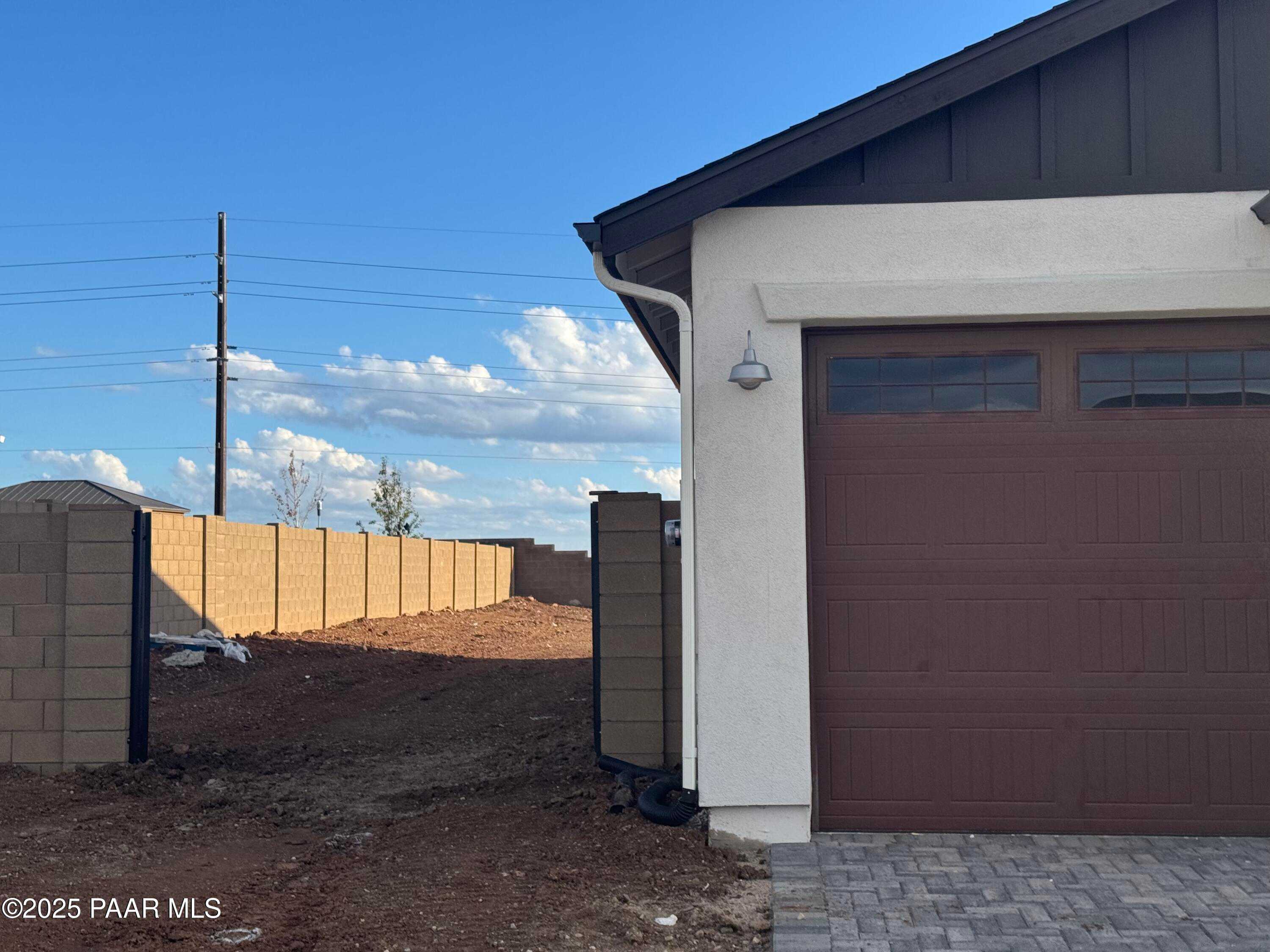 Modern 4-car garage with brown doors on white stucco Evermore Homes The Sunrise A in Morningstar, Prescott Valley, Arizona, block fence backdrop