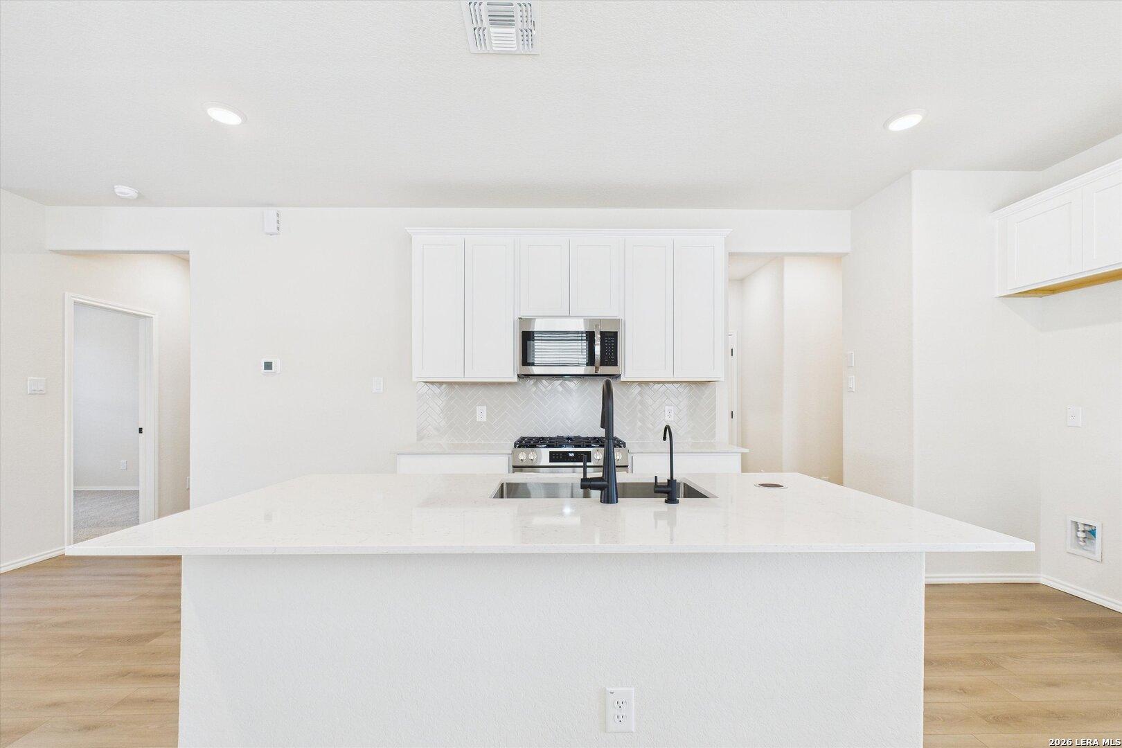 Modern white kitchen with large island, stainless steel appliances, and open layout in The Gillian B floor plan, San Antonio, TX