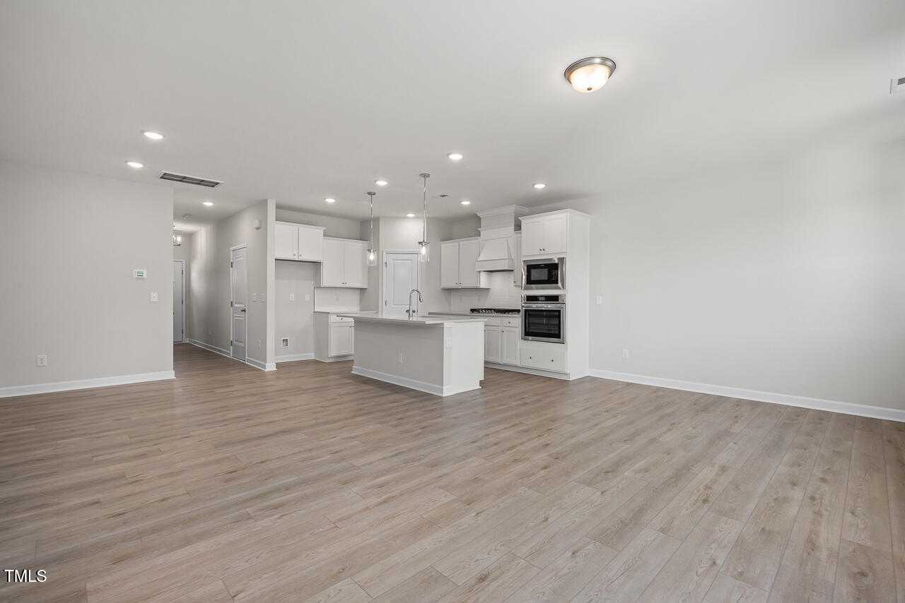 Modern white kitchen with large island, stainless oven, recessed lights, hardwood floors in The Warren by Davidson Homes, Fuquay-Varina, NC