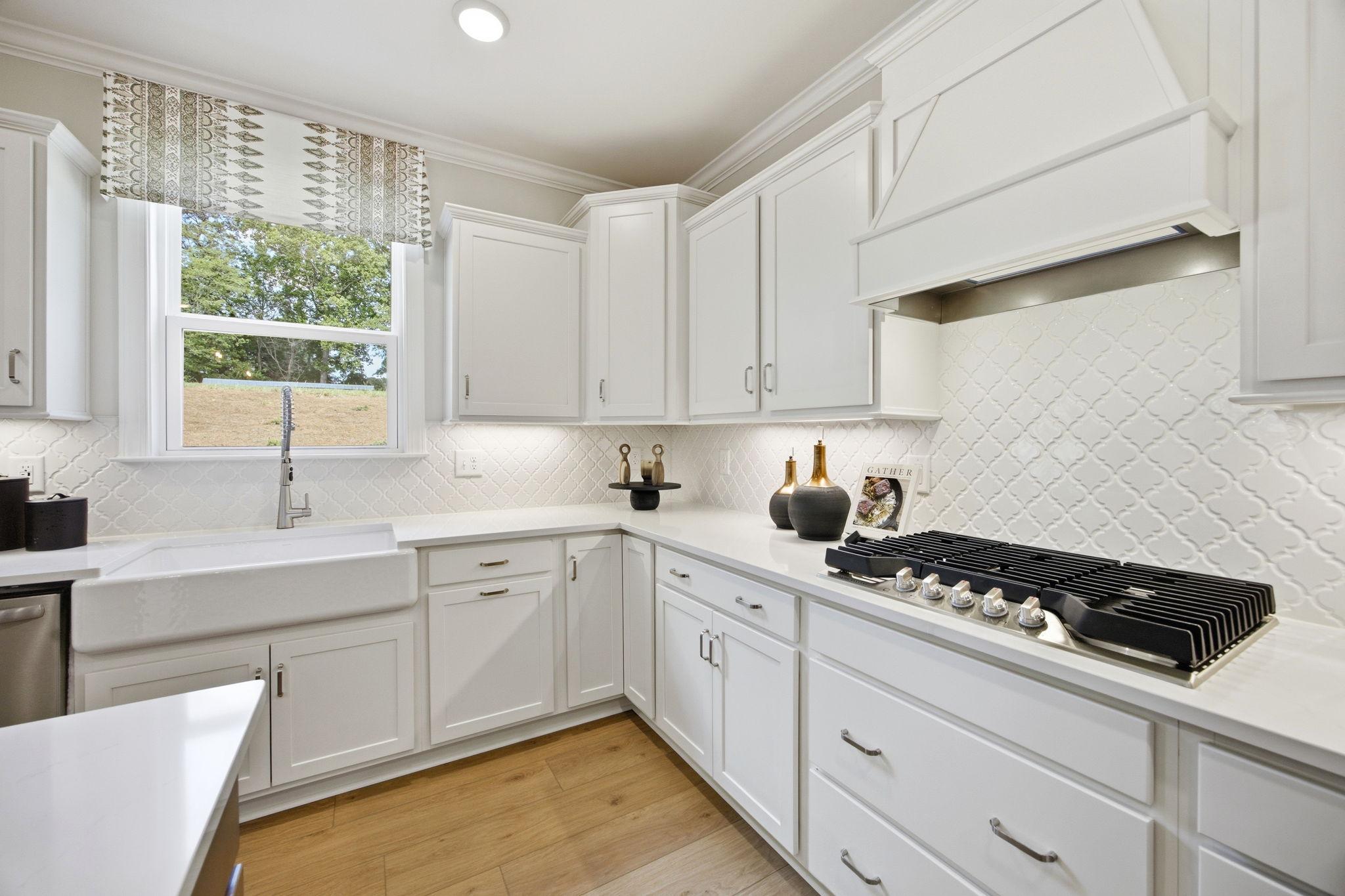 Spacious white kitchen at Enclave at Belmont in NC with farmhouse sink, herringbone tile backsplash, and gas range
