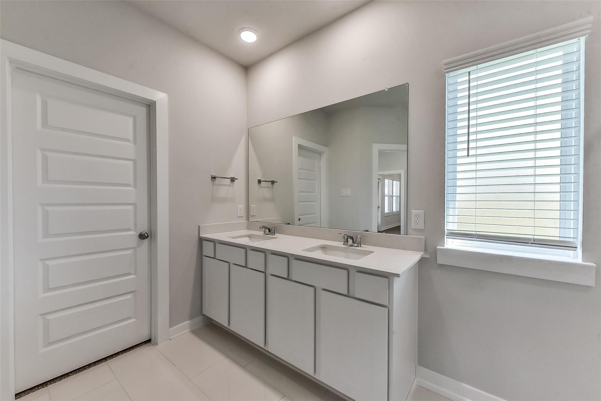 Modern double vanity bathroom with white shaker cabinets, quartz counters, and large mirror in Davidson Homes The Costa B, Dayton, Texas