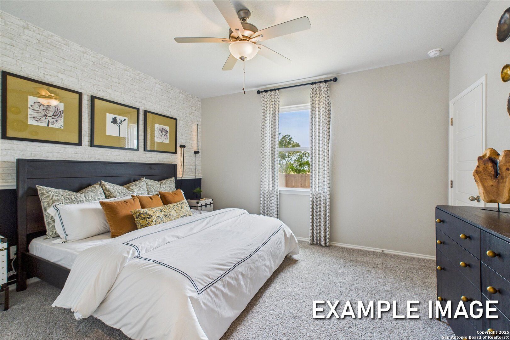 Cozy bedroom with king bed, beige brick accent wall, ceiling fan, and sheer curtains in Davidson Homes The Sabine C, Agave, San Antonio