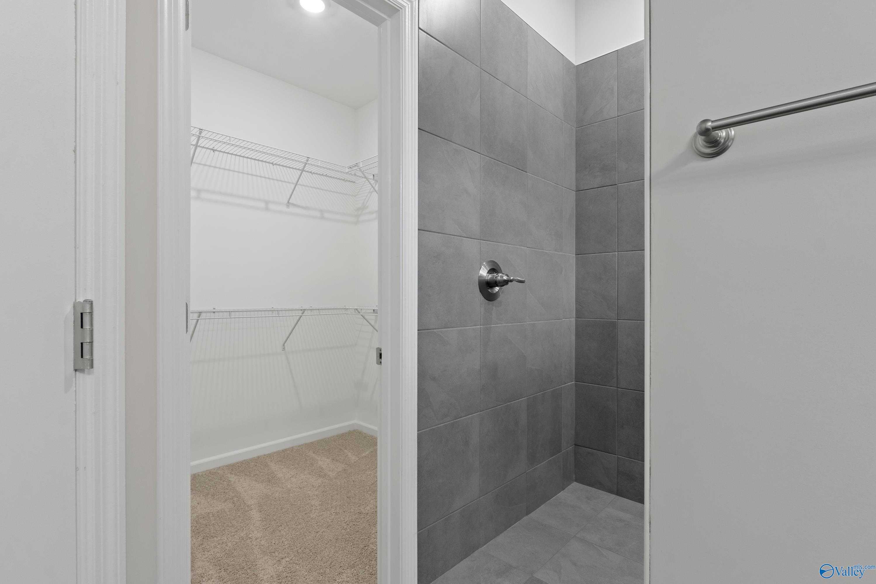 Modern master bathroom featuring gray tiled walk-in shower and adjacent spacious closet with wire shelving in Davidson Homes The Dorado, Athens AL