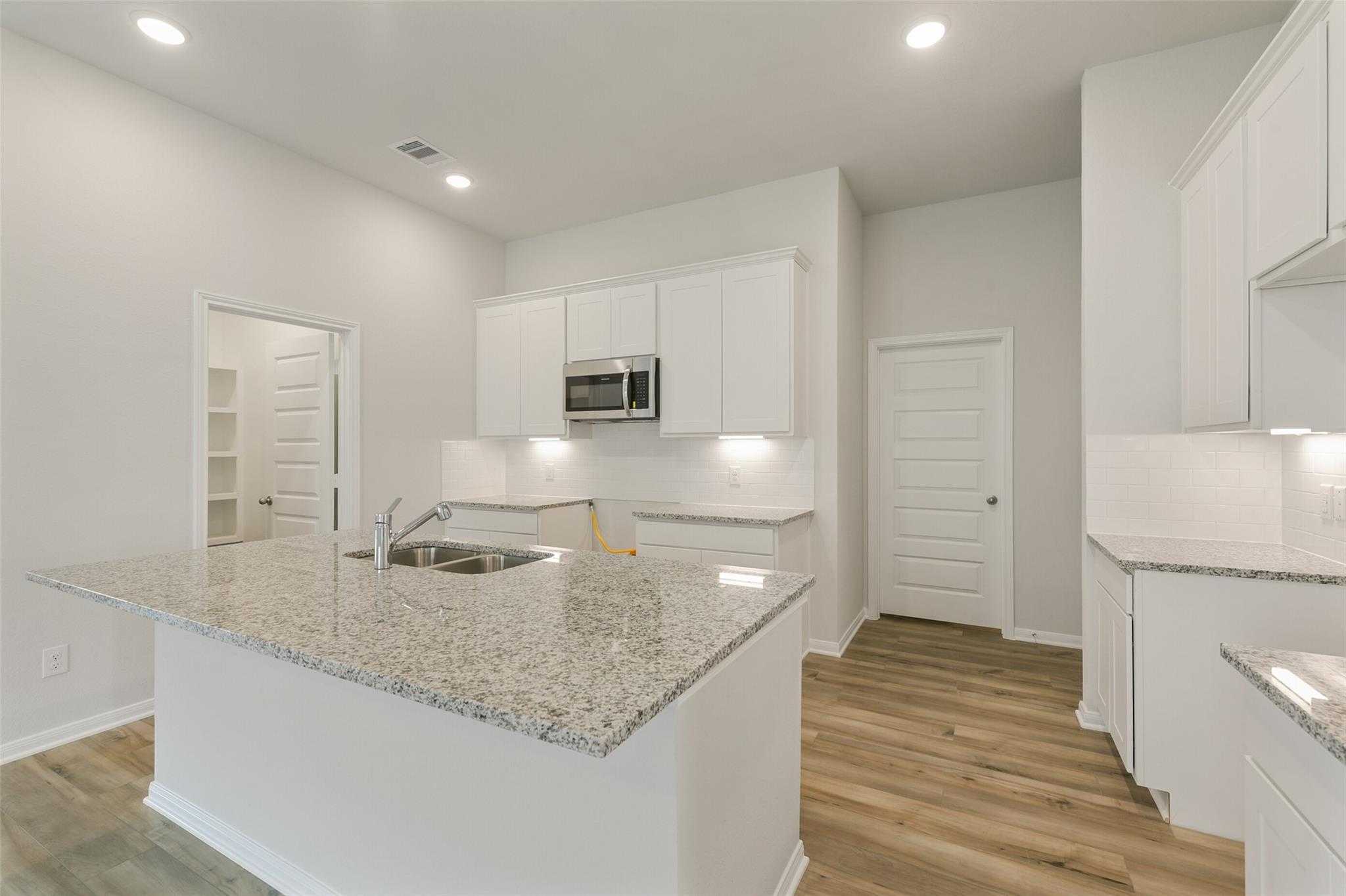 Modern kitchen featuring white cabinets, granite island sink, and stainless microwave in Davidson Homes The Laguna B, Dayton, Texas