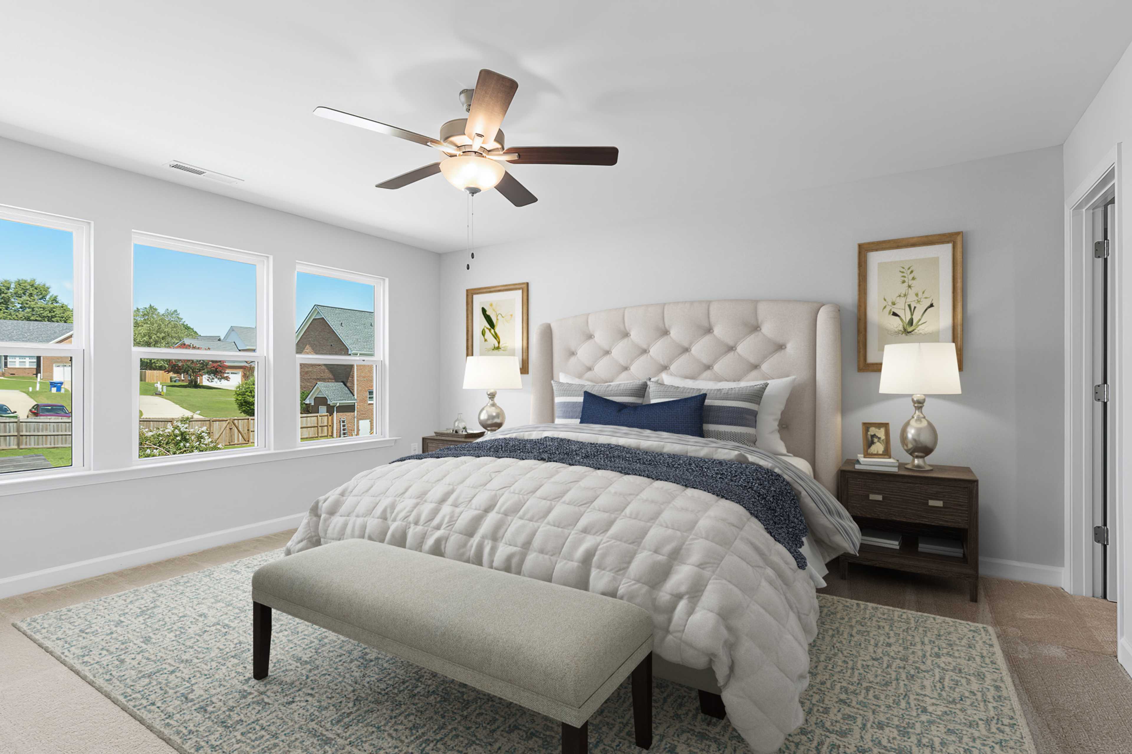 Primary bedroom at Enclave at Belmont in Belmont NC with tufted upholstered bed, ceiling fan, and large window views