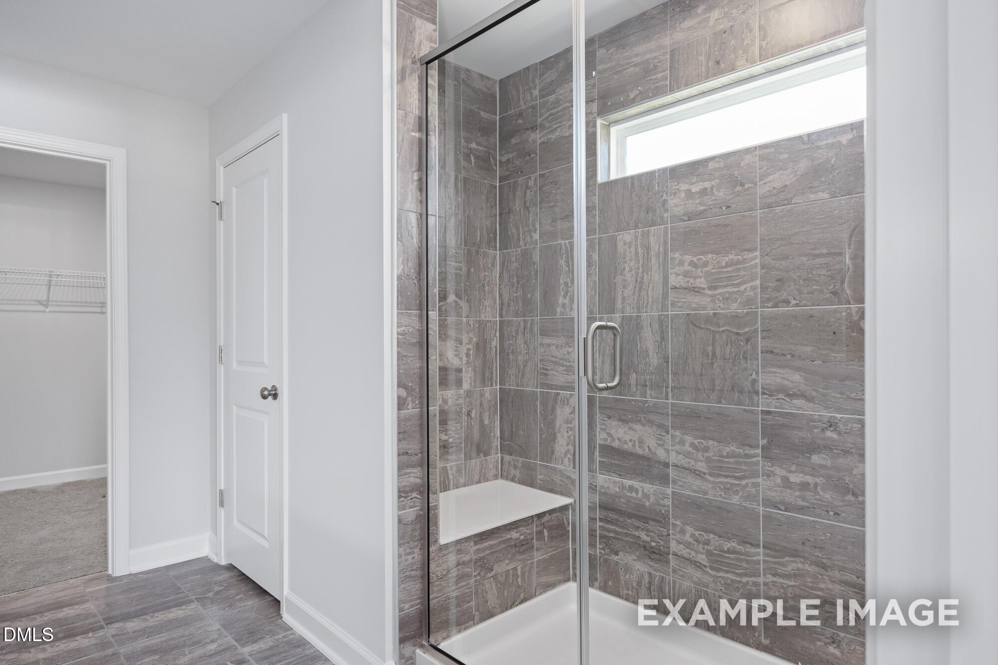 Modern frameless glass shower with gray tile walls, bench seat, and window in master bath, adjacent walk-in closet in Davidson Homes Hickory II B, Lillington NC