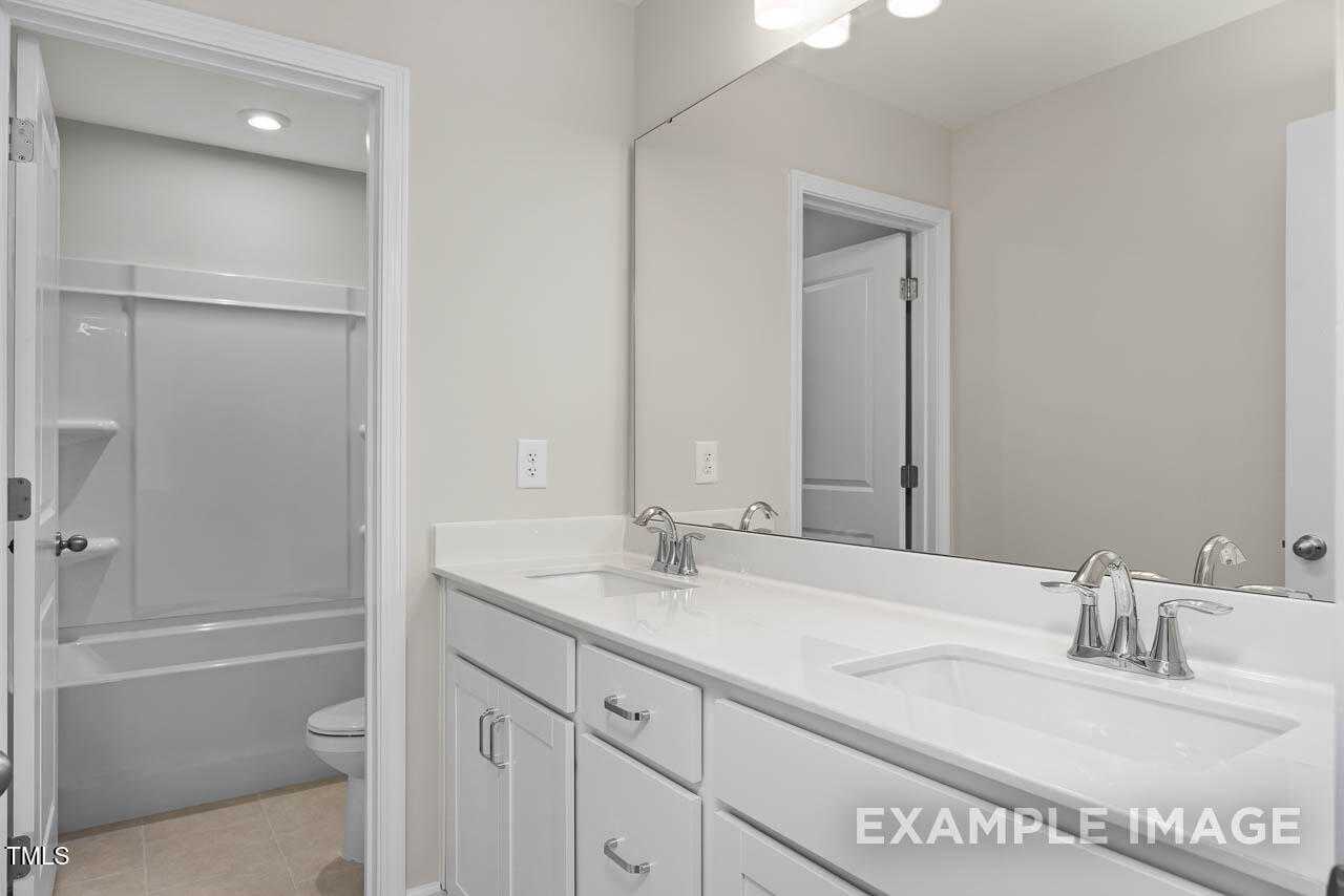 Bright master bathroom with double vanity, tub-shower combo, and large mirror in Davidson Homes Hickory II B, Lillington NC