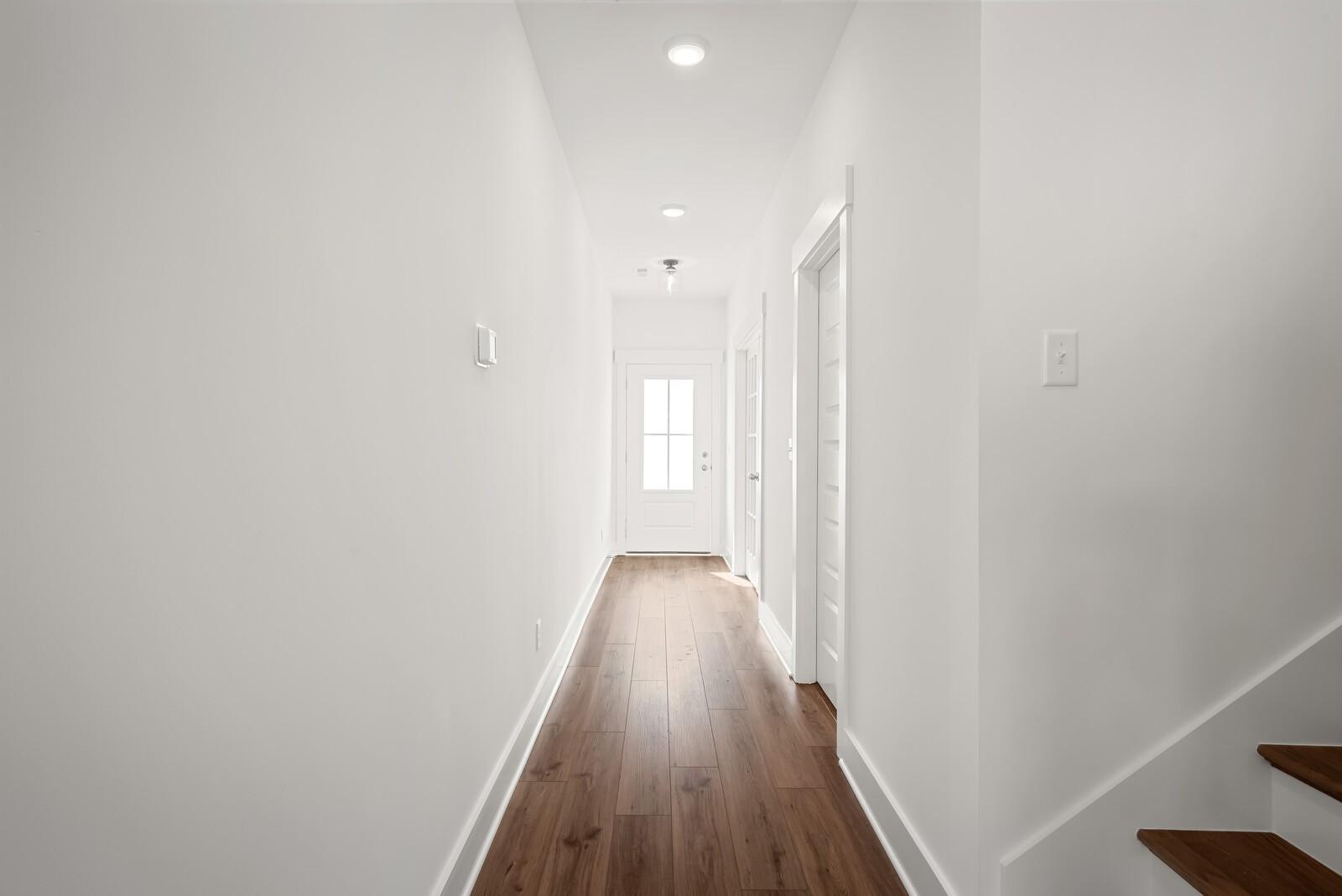 Bright white hallway with hardwood floors, doors, and staircase in Davidson Homes The Logan C, Gallatin, Tennessee