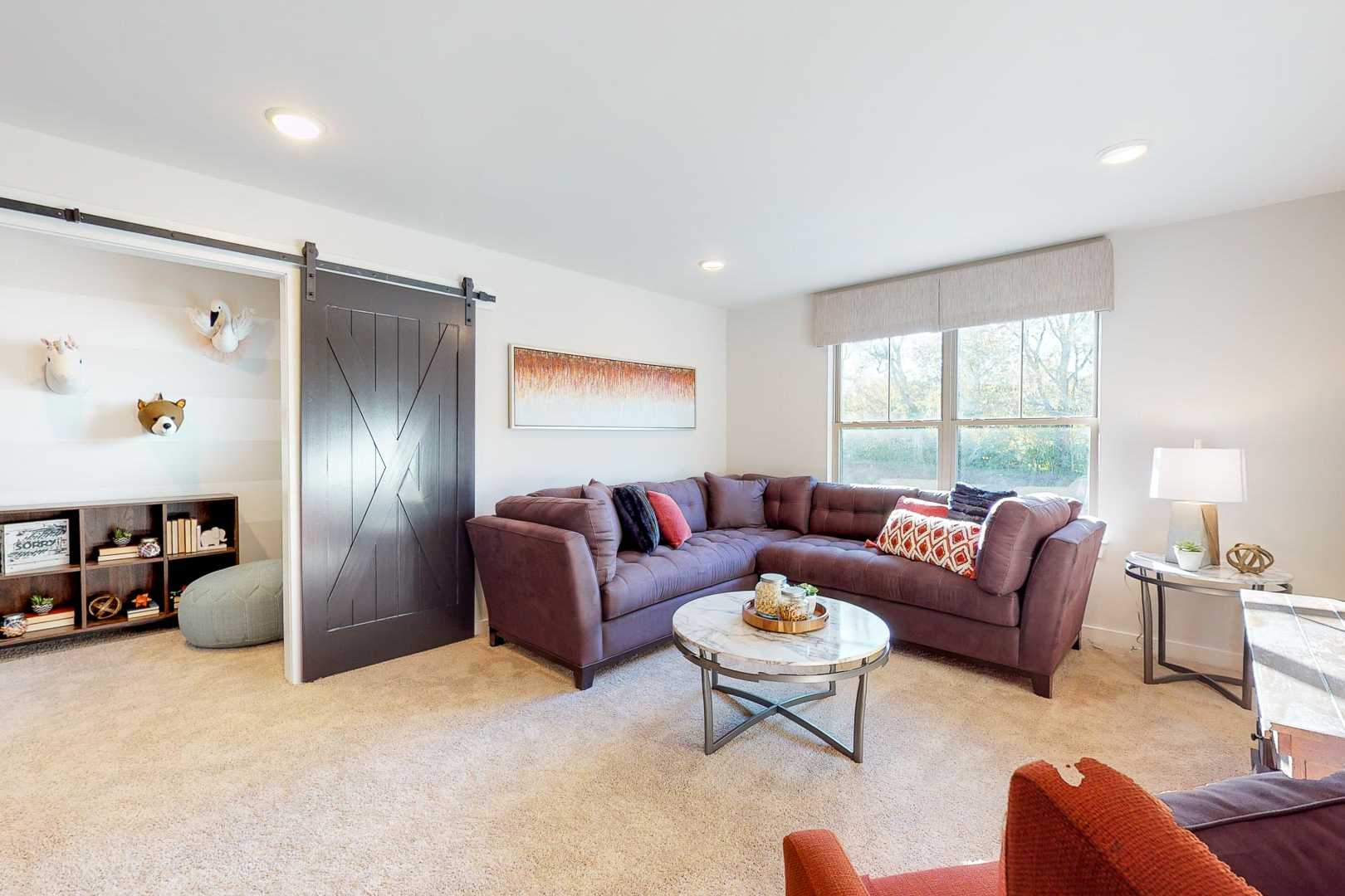 Cozy family room at Liberty Creek in Gallatin TN with sliding barn door, plush sectional sofa, whimsical decor, and modern accents by Davidson Homes