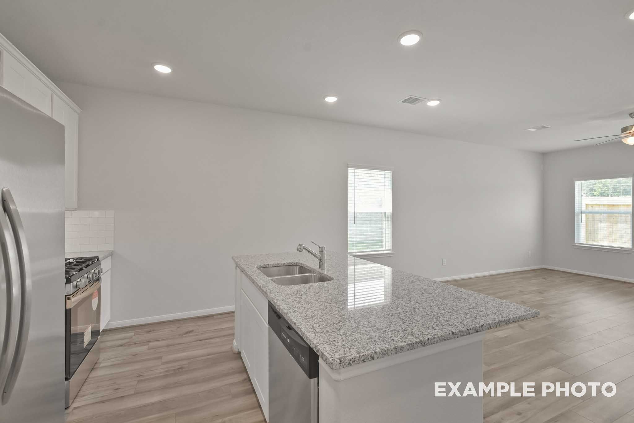 Spacious kitchen in The Comal floor plan with white cabinets, granite island sink, stainless appliances, open to living area