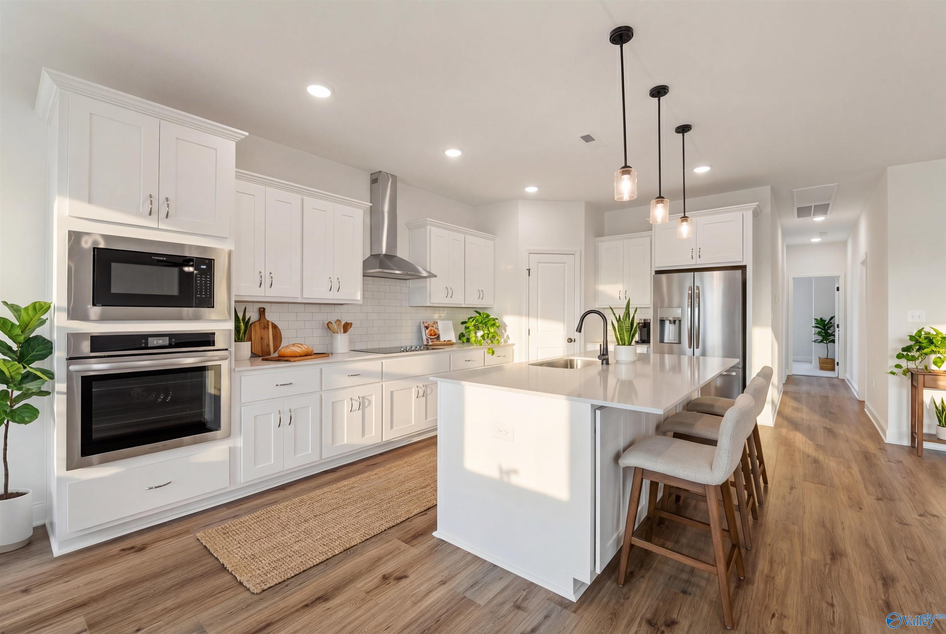 Modern white kitchen island with stainless double ovens, pendant lights, and plants in Davidson Homes The Rockford B, Toney, AL