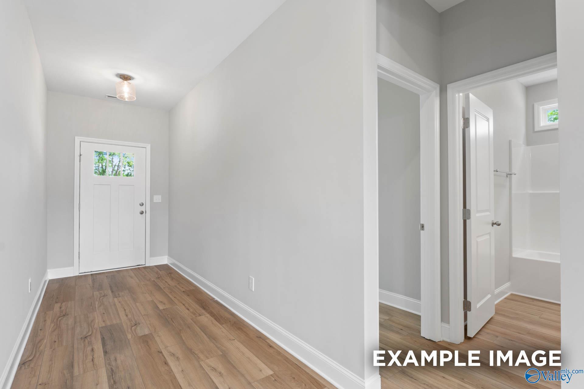 Bright hallway featuring white front door with sidelights, hardwood floors, and open bathroom in 5-bedroom Davidson Homes Chelsea A, Meridianville AL