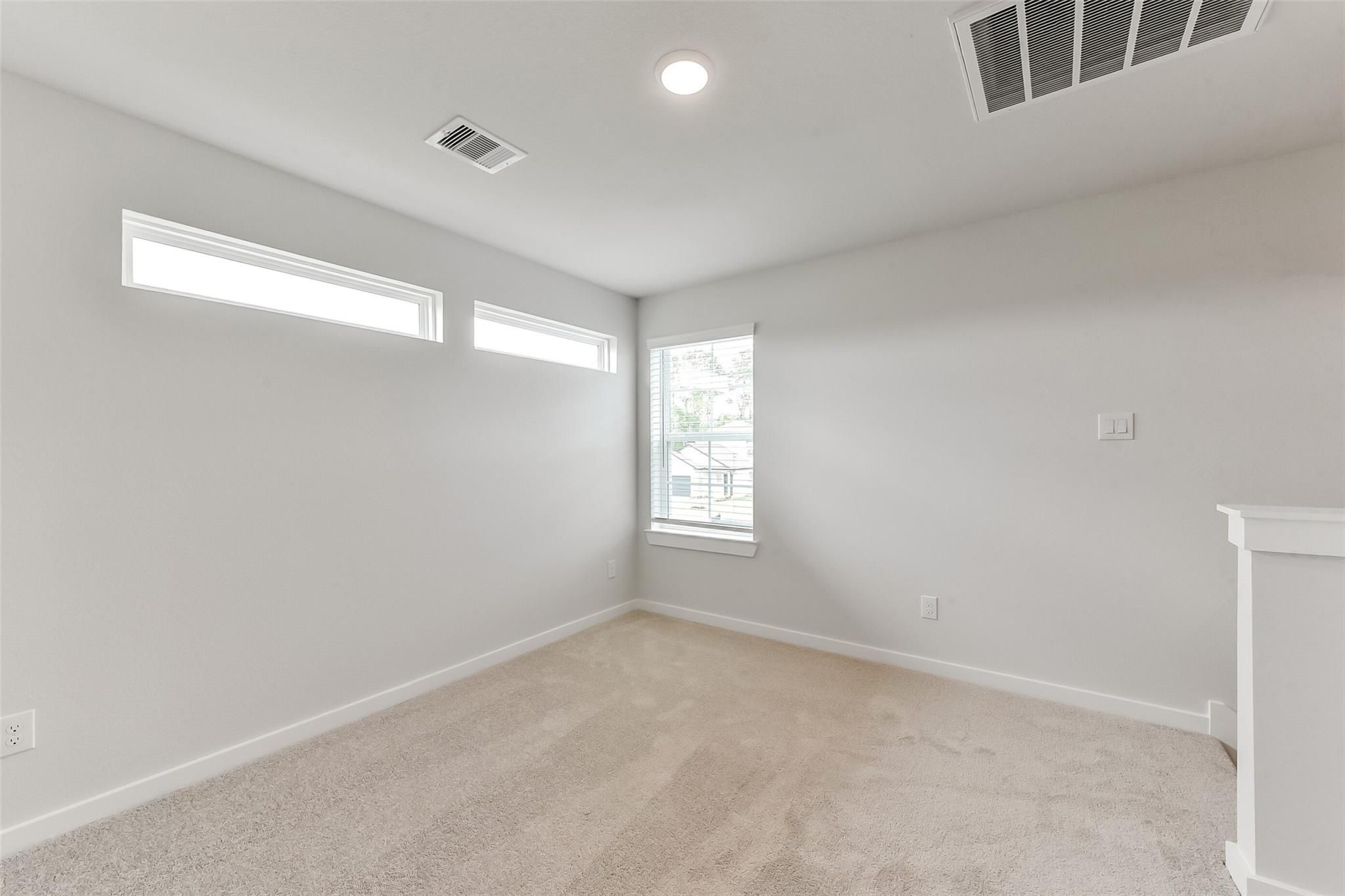Bright upstairs bedroom with gray walls, beige carpet, large windows, and railing in The Sabine F home, Dayton, Texas