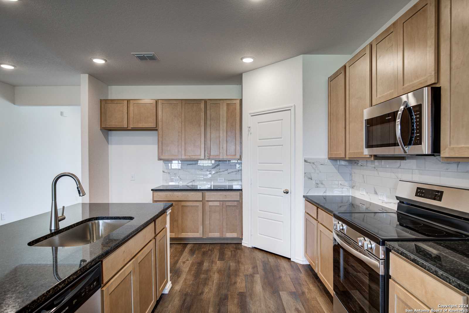 Modern kitchen featuring oak cabinets, granite island sink, stainless microwave and oven in Davidson Homes The Douglas D, Seguin, Texas