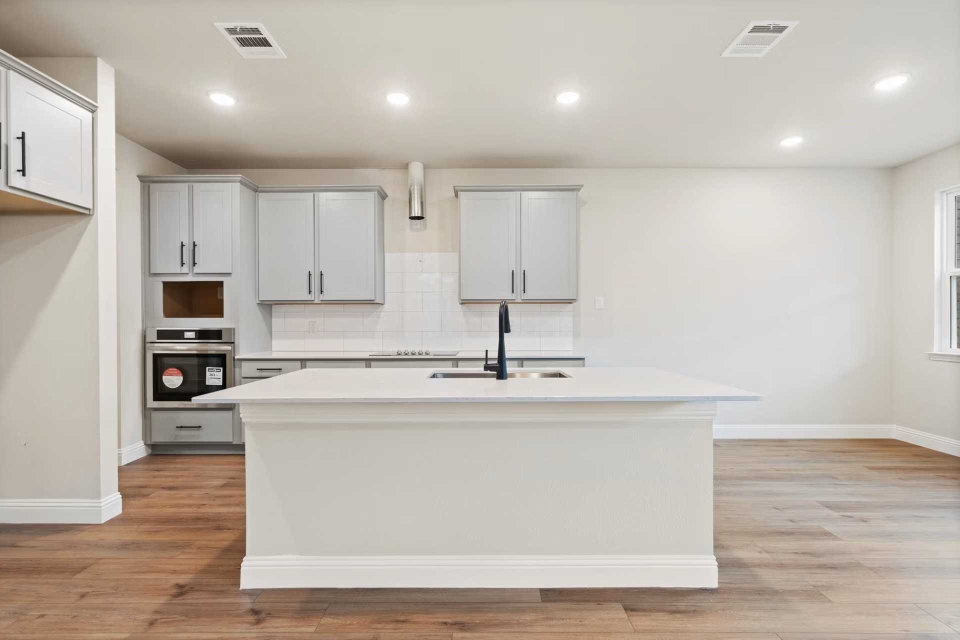 Modern white kitchen island with sink, subway tile backsplash, and built-in oven in Davidson Homes The Wake D, Wylie, Texas