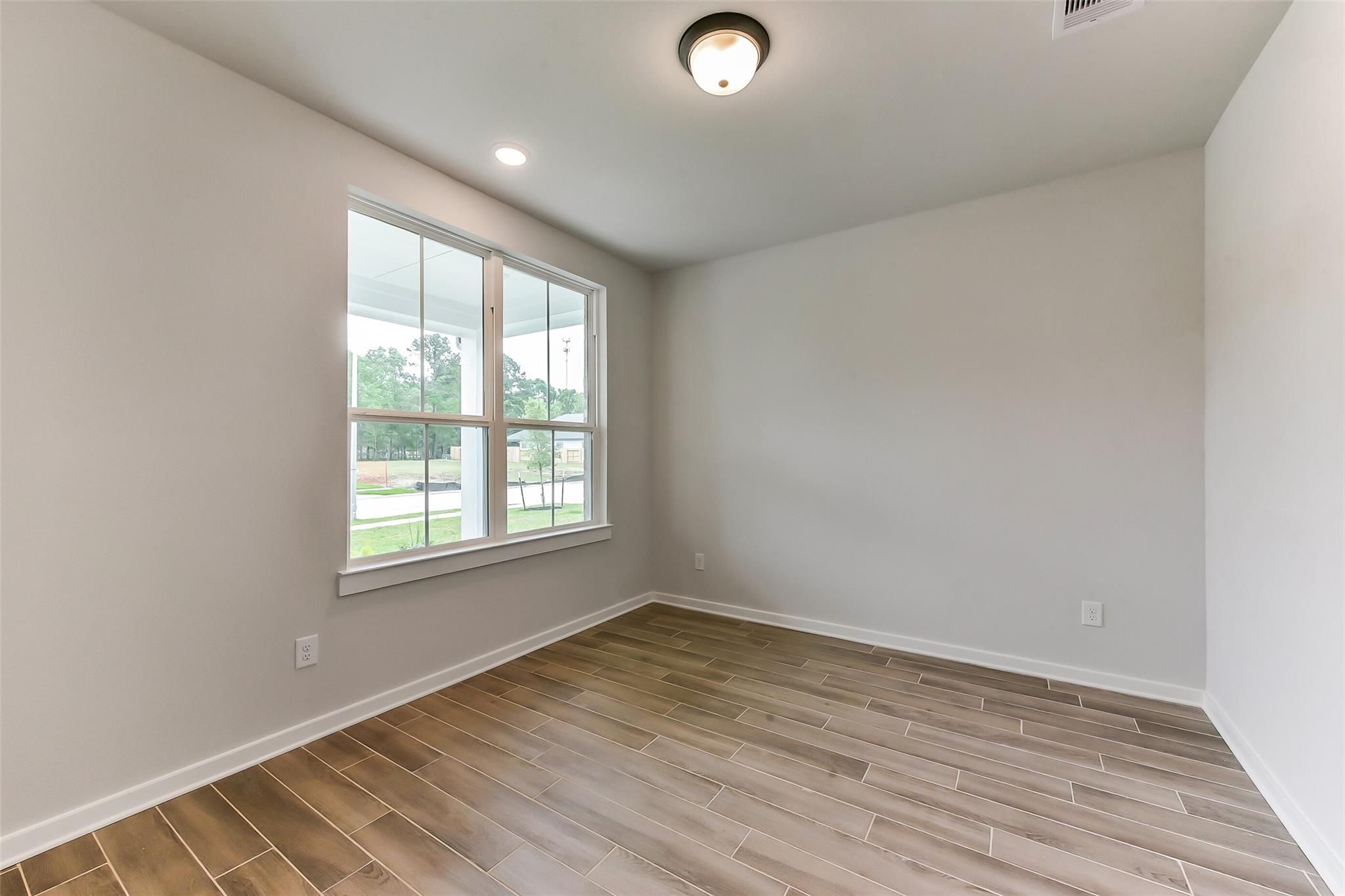 Bright living room with large windows, wood-look tile floors, and natural light in Davidson Homes Sequoia C, Crosby, Texas