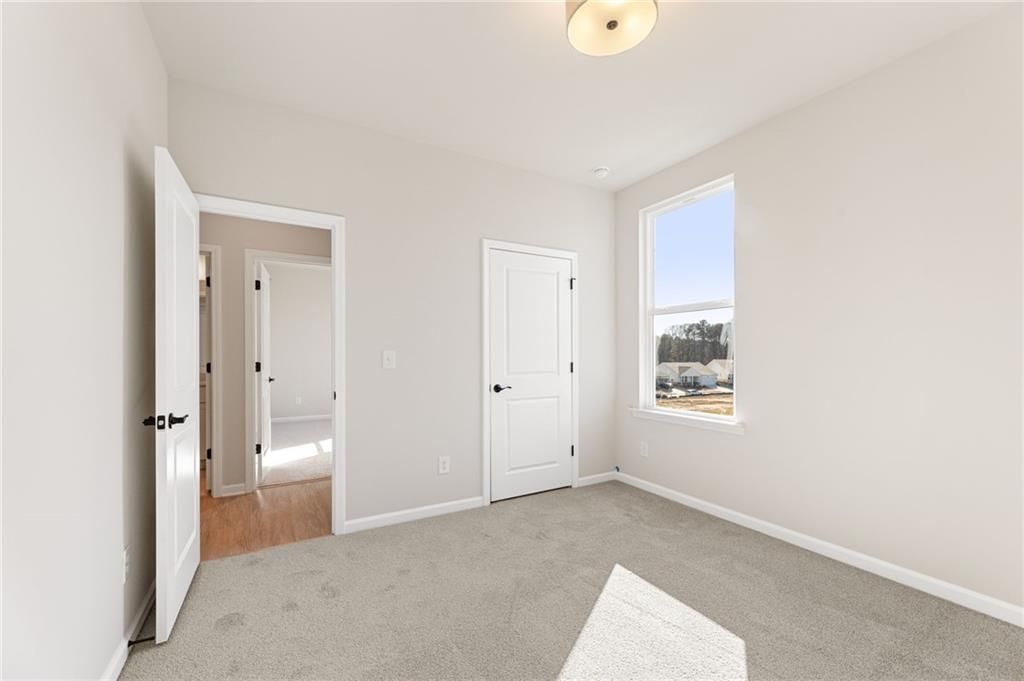Bright secondary bedroom with beige walls, gray carpet, double doors, and sunny window in Davidson Homes The Glenwood C, Loganville, GA