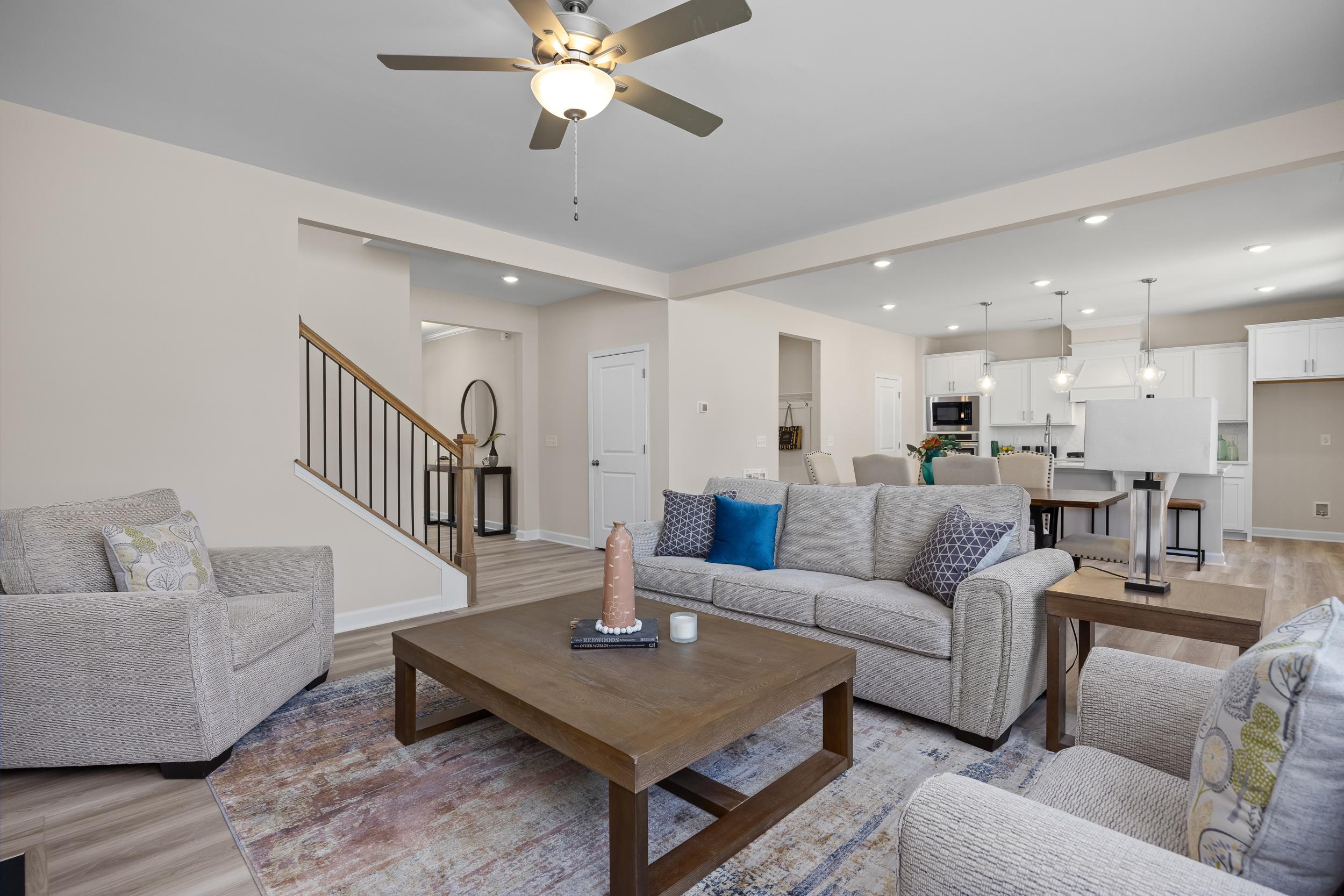 Open-concept living room at Montrose in Aberdeen, NC with gray sofas, wooden coffee table, ceiling fan, and open kitchen