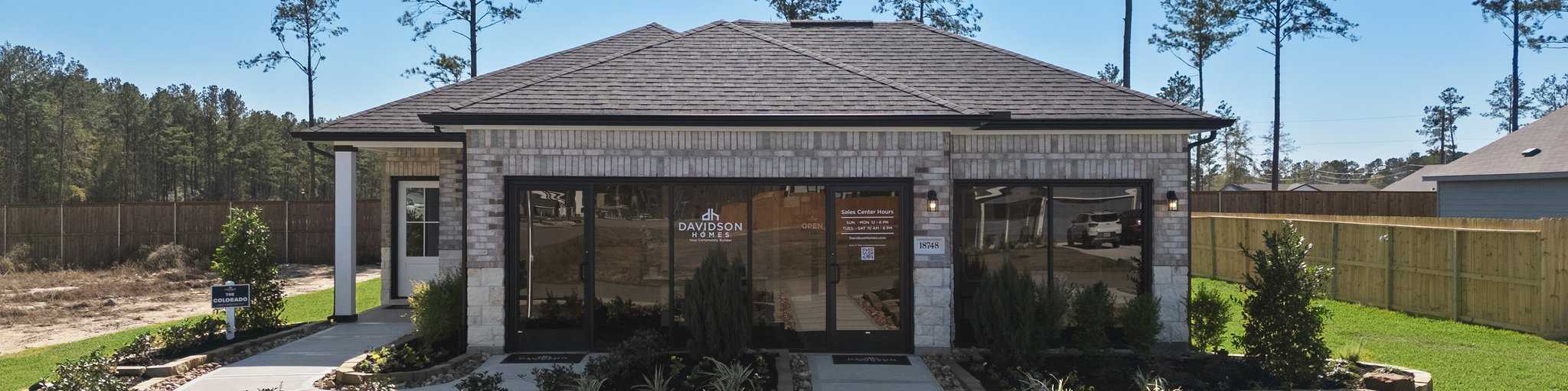 Davidson Homes sales center at Spring Branch Crossing in Conroe, Texas, featuring a landscaped walkway and brick exterior.