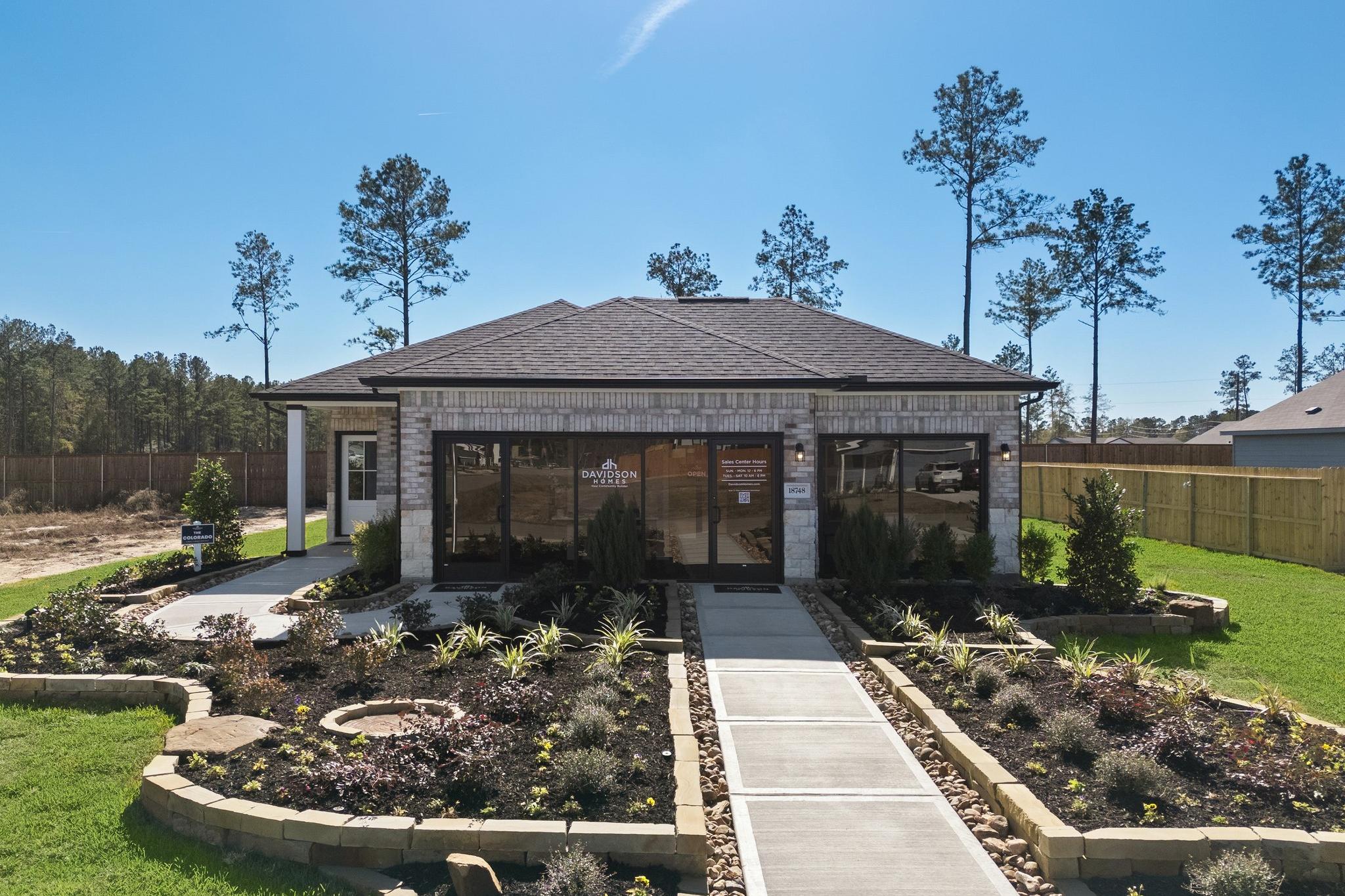 Stone and brick model home exterior at Spring Branch Crossing in Conroe Texas with landscaped gardens and walkway