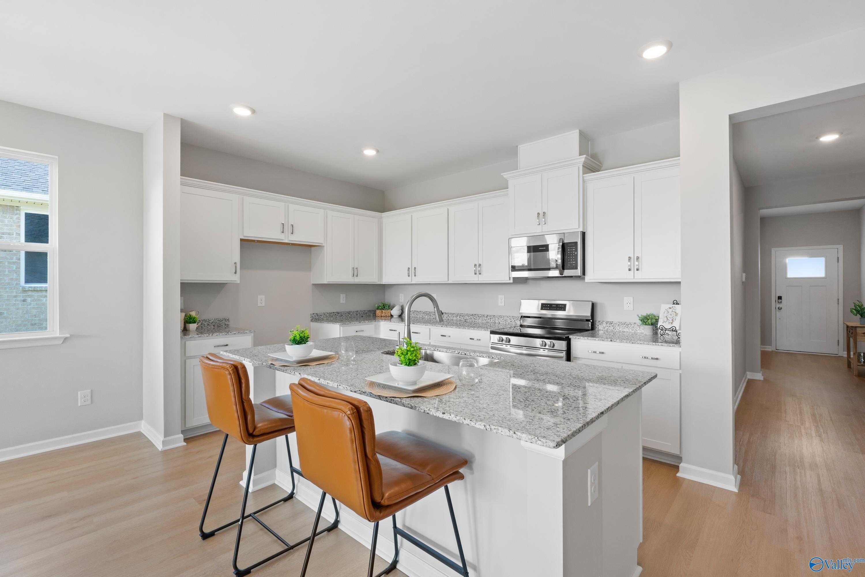 Modern white kitchen with granite island, stainless steel appliances, and leather bar stools in Davidson Homes The Aurora, Fayetteville, TN