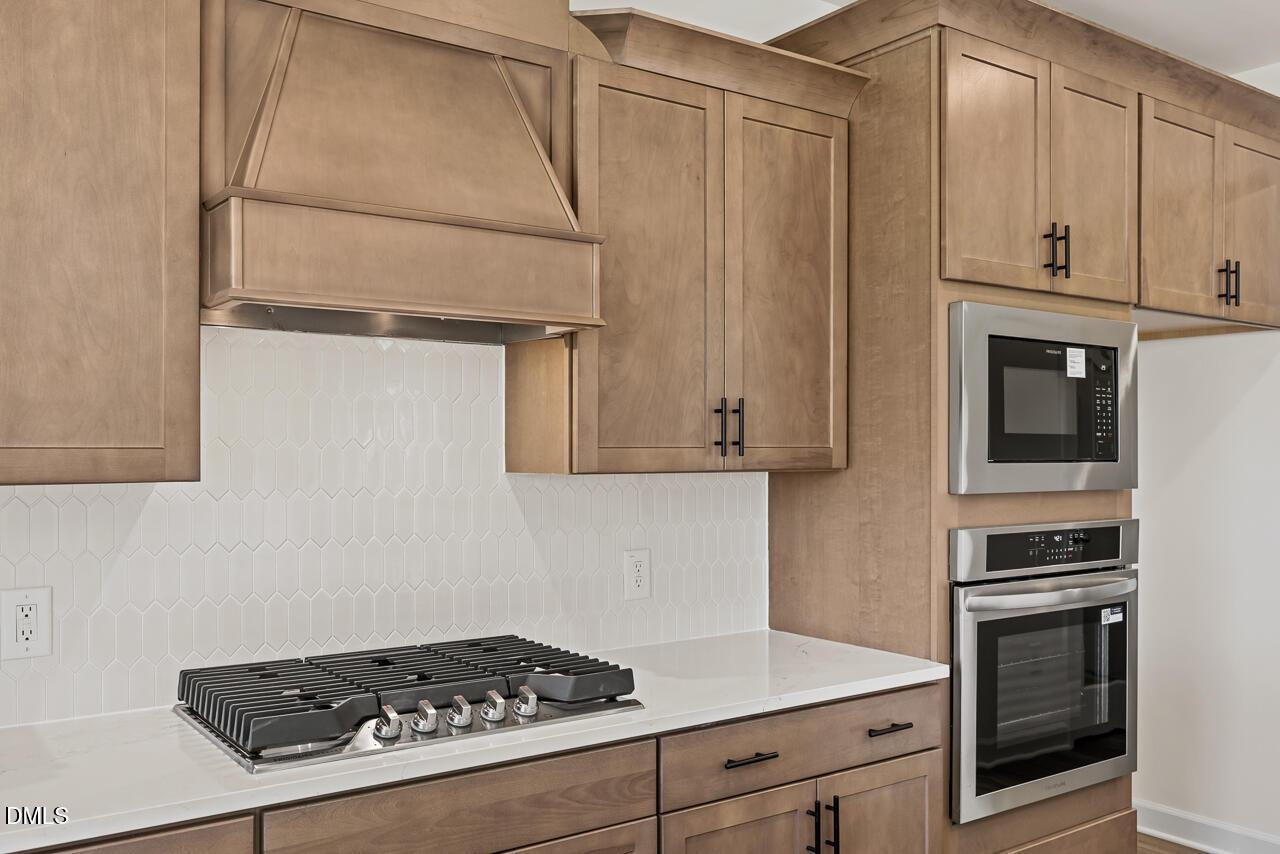 Modern kitchen with wood cabinets, hexagon tile backsplash, gas cooktop, and stainless built-in oven in Davidson Homes Lillington NC