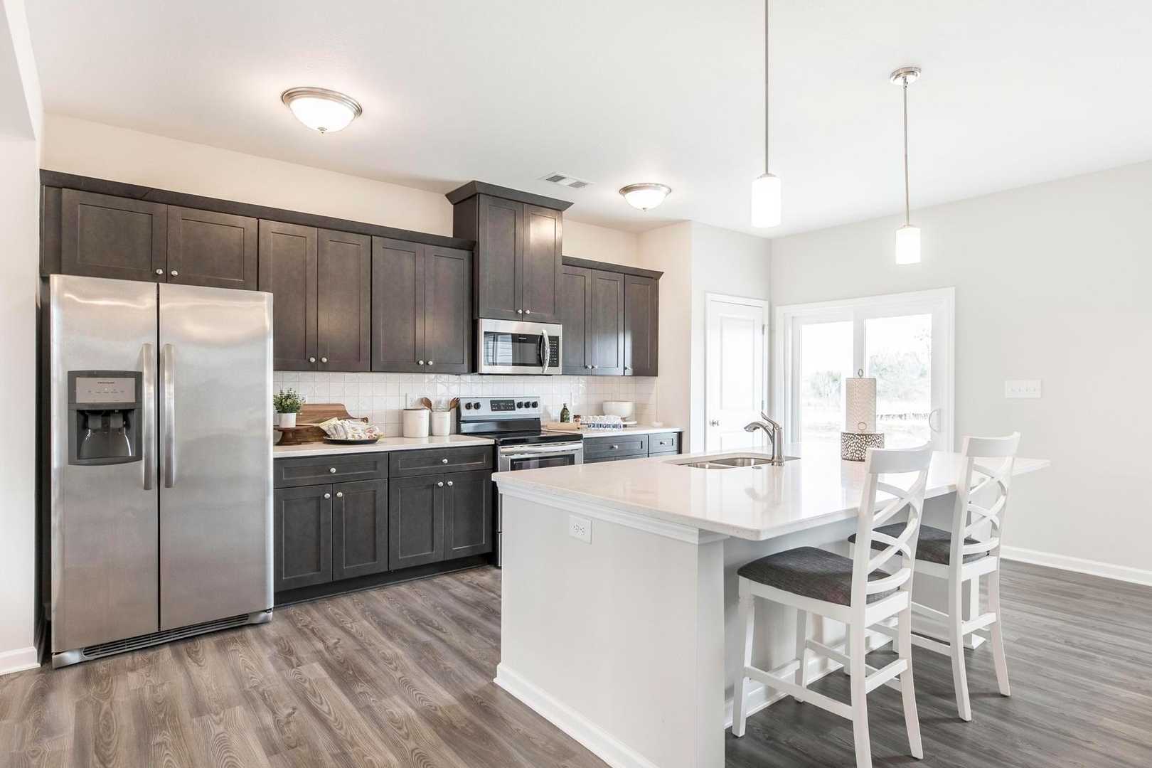 Modern kitchen with dark shaker cabinets, stainless appliances, white island and bar stools at Cape Reserve in Donahue Ridge, Auburn AL