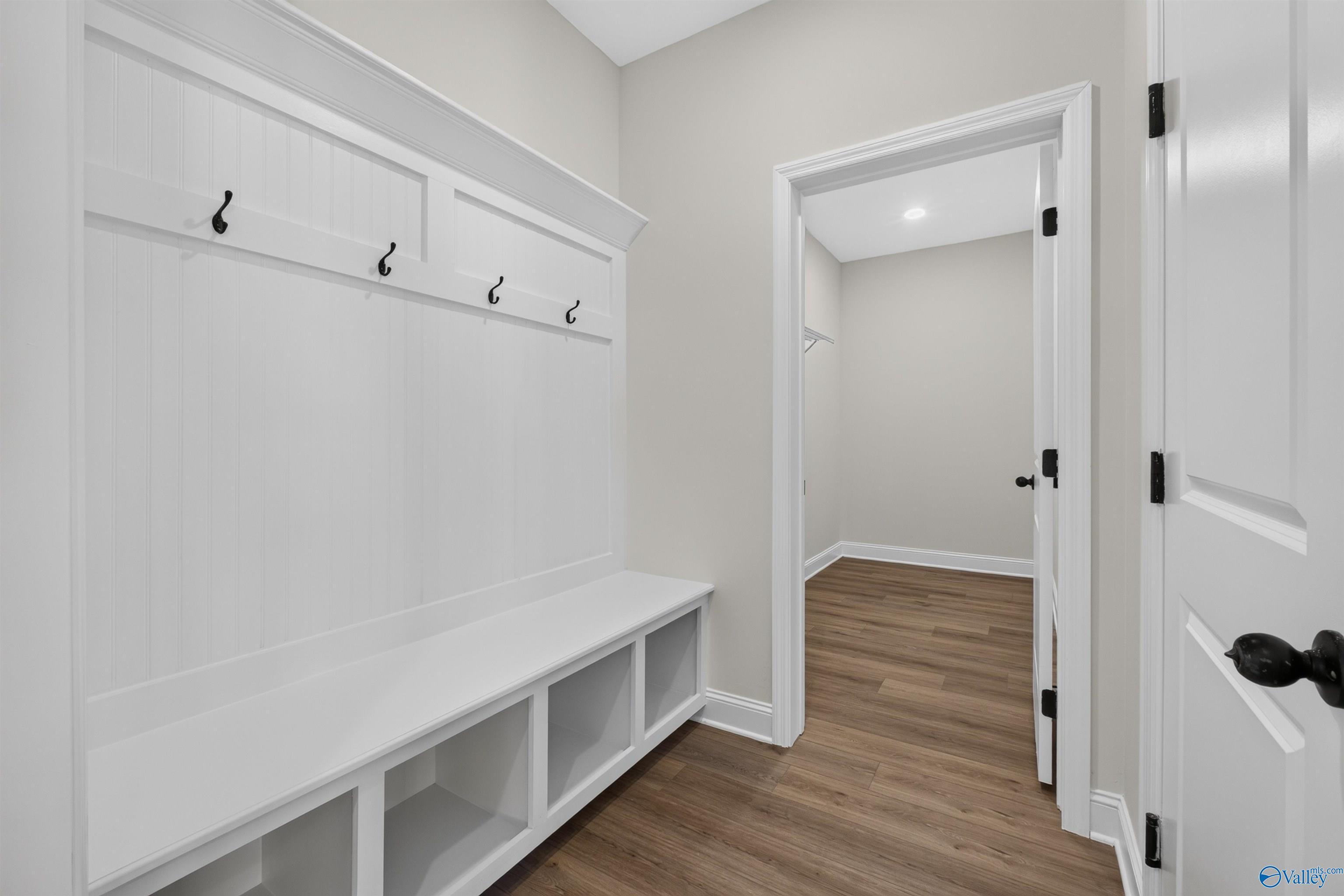 White mudroom drop zone with beadboard wall, hooks, storage bench, and wood-look flooring in Davidson Homes Ashport L, New Market, AL