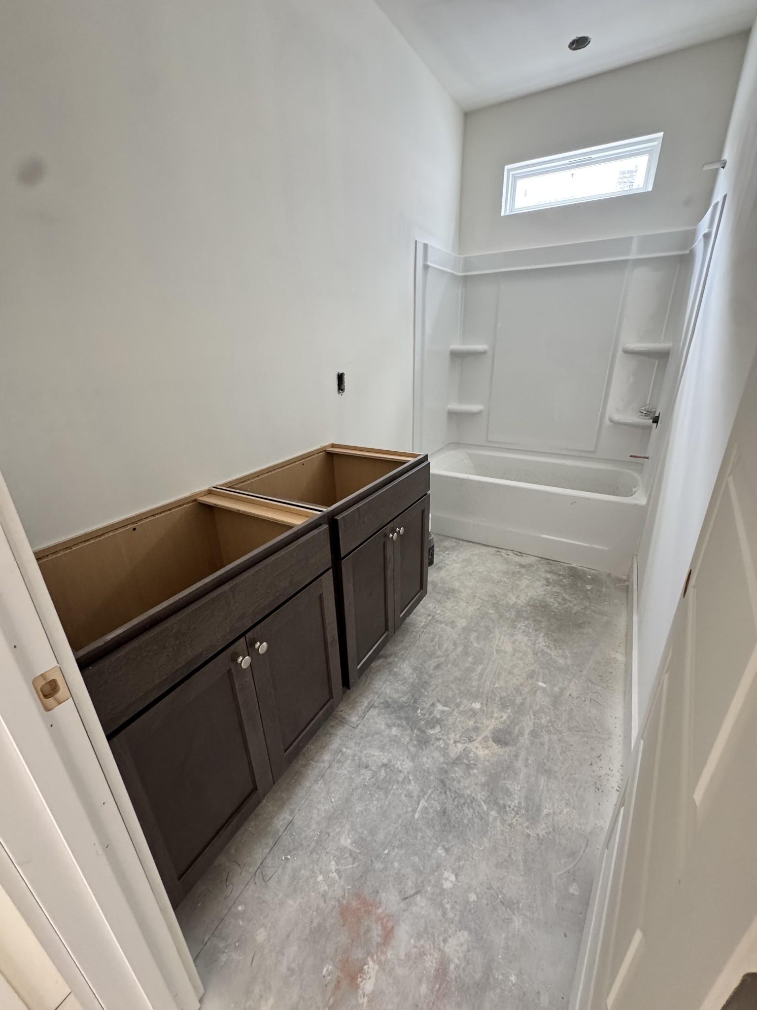 Unfinished bathroom with dual wood vanity cabinets, white alcove bathtub, and shower niche in Davidson Homes Cottonwood E, Gallatin, TN