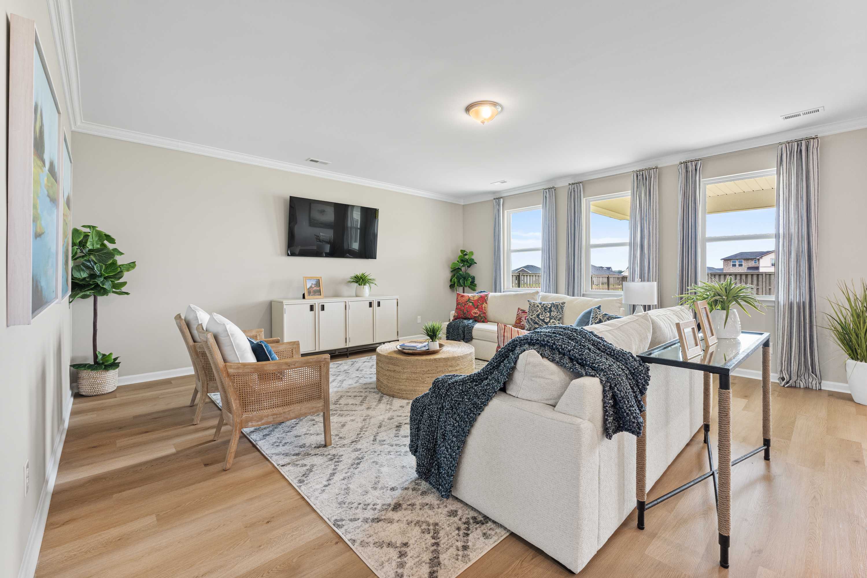 Spacious living room in Anderson Farm Athens AL with hardwood floors, white sectional sofa, rattan armchair, and potted plants