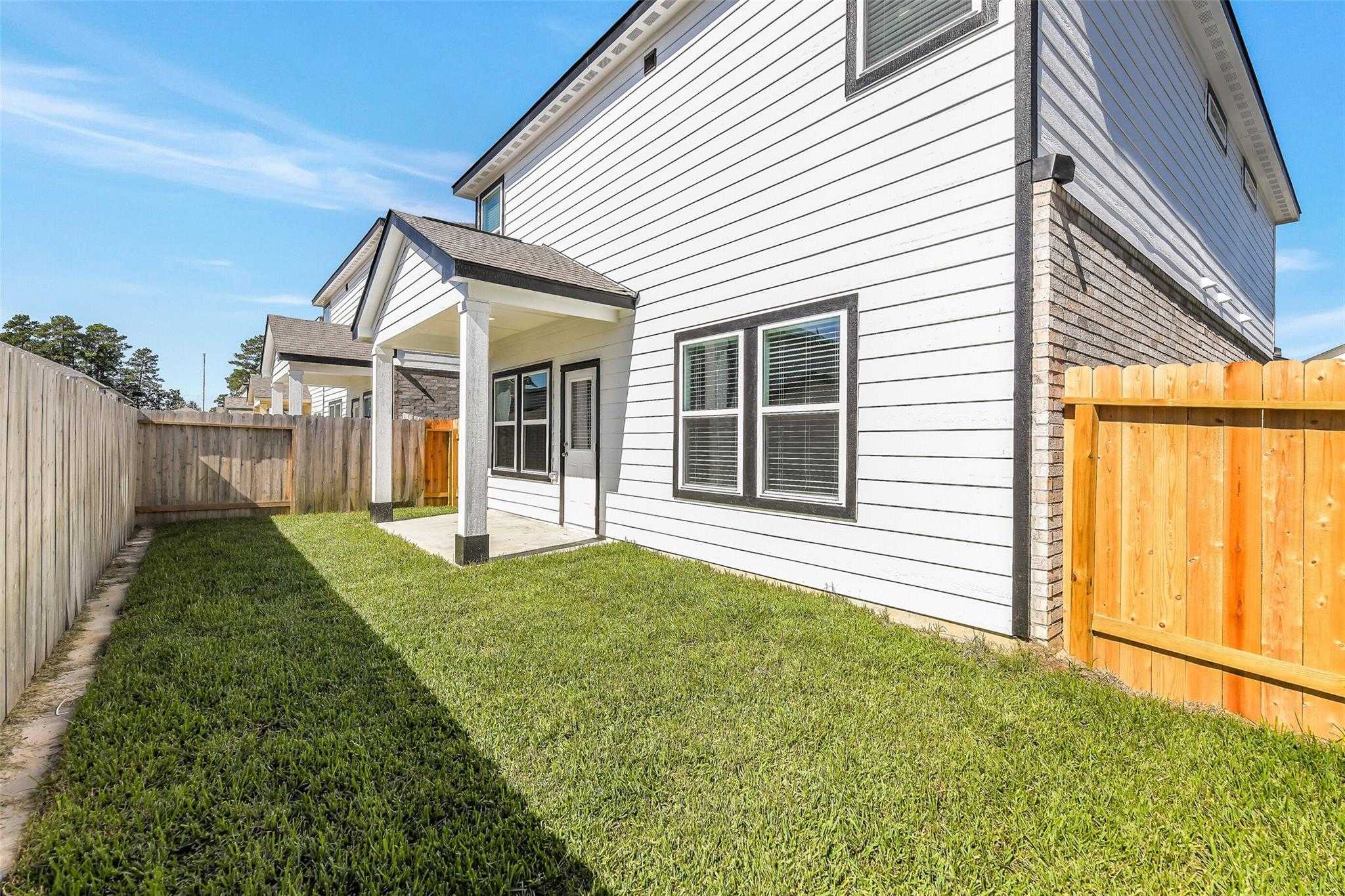 Two-story white home side view with covered porch, double windows, lush green lawn, and cedar fence in Magnolia, Texas