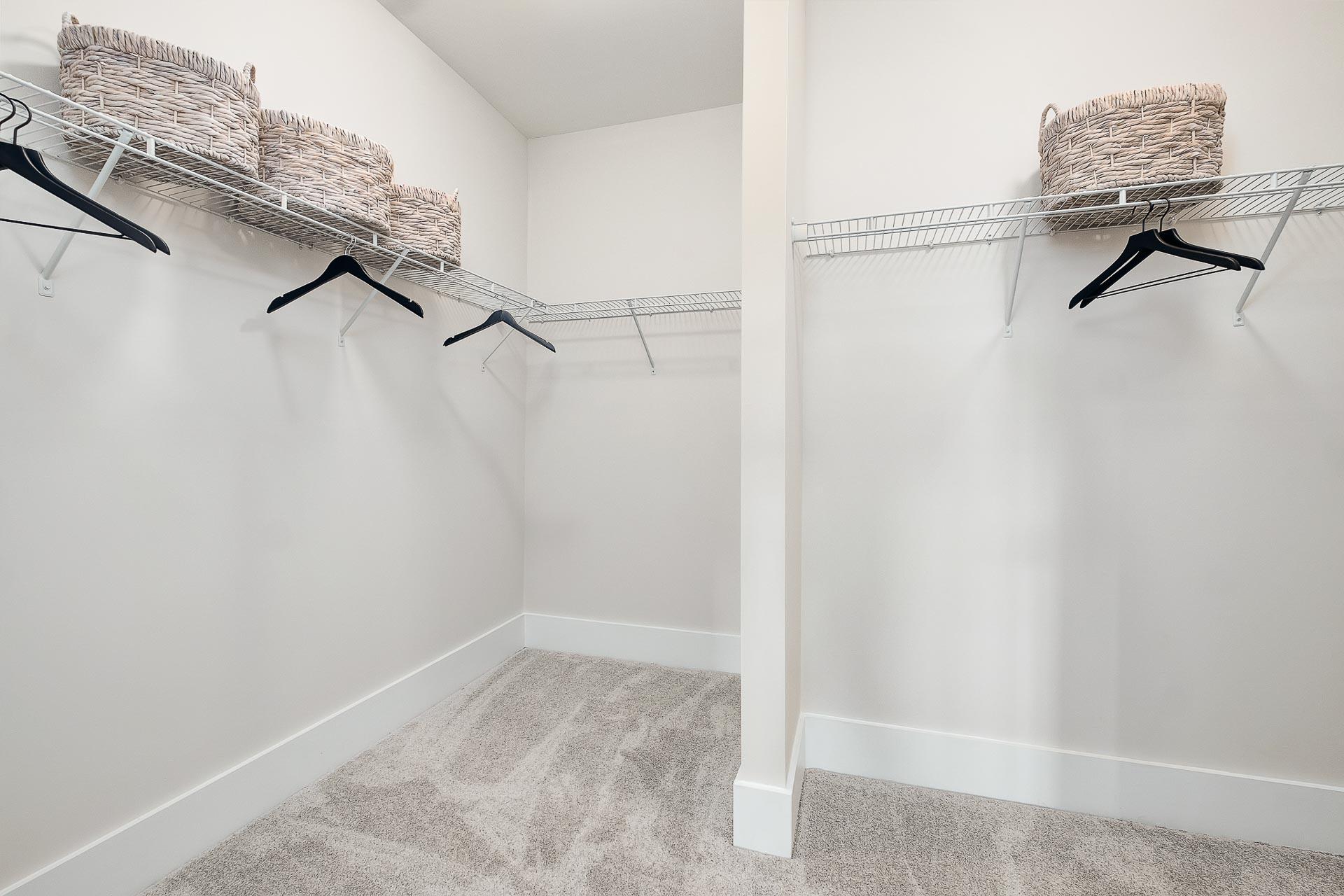 Spacious walk-in closet in The Everett featuring wire shelving, hanging rods, wicker baskets, neutral walls, and carpeted floor