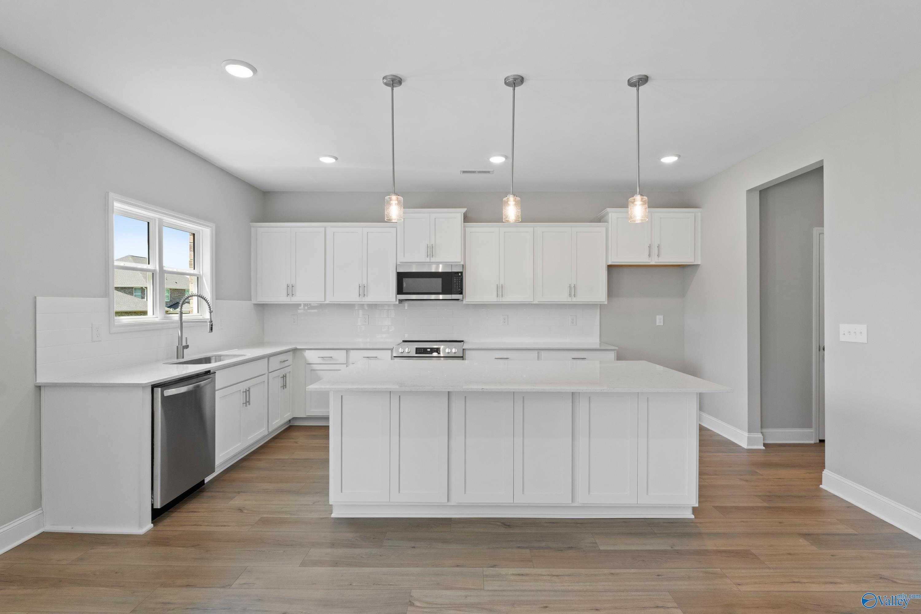 Modern white shaker kitchen with large island, stainless steel appliances, and hardwood floors in Davidson Homes Chelsea B, New Market, AL