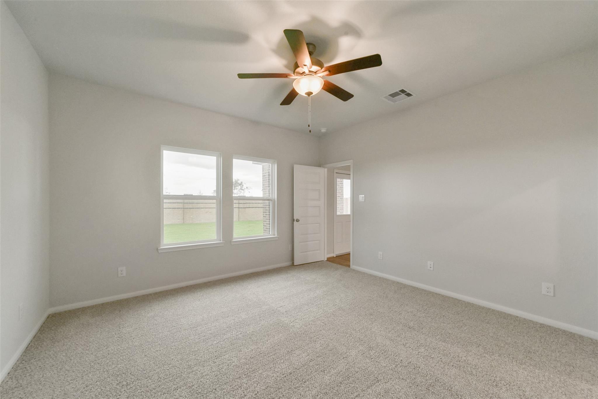 Bright secondary bedroom with ceiling fan, large windows, and carpet in Davidson Homes The San Marcos E, Beasley, Texas
