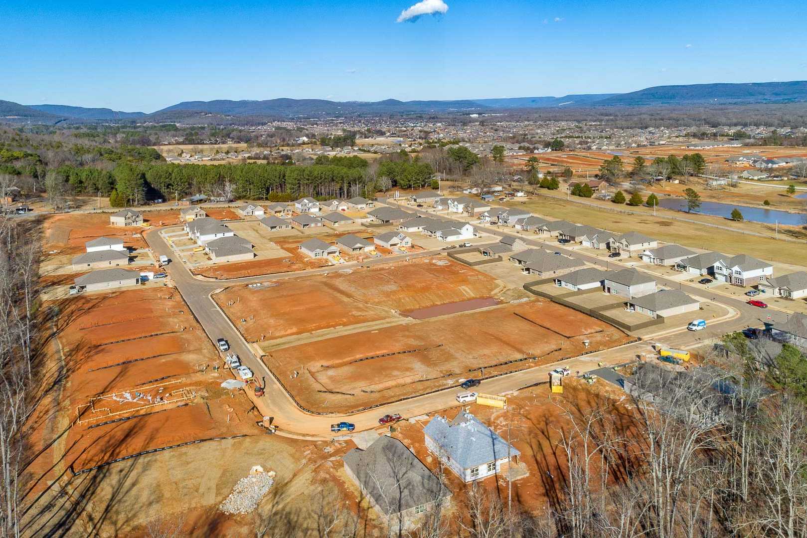 Aerial drone view of Monteagle Cove in Owens Cross Roads AL, new Davidson Homes under construction on red clay lots with pond and wooded hills