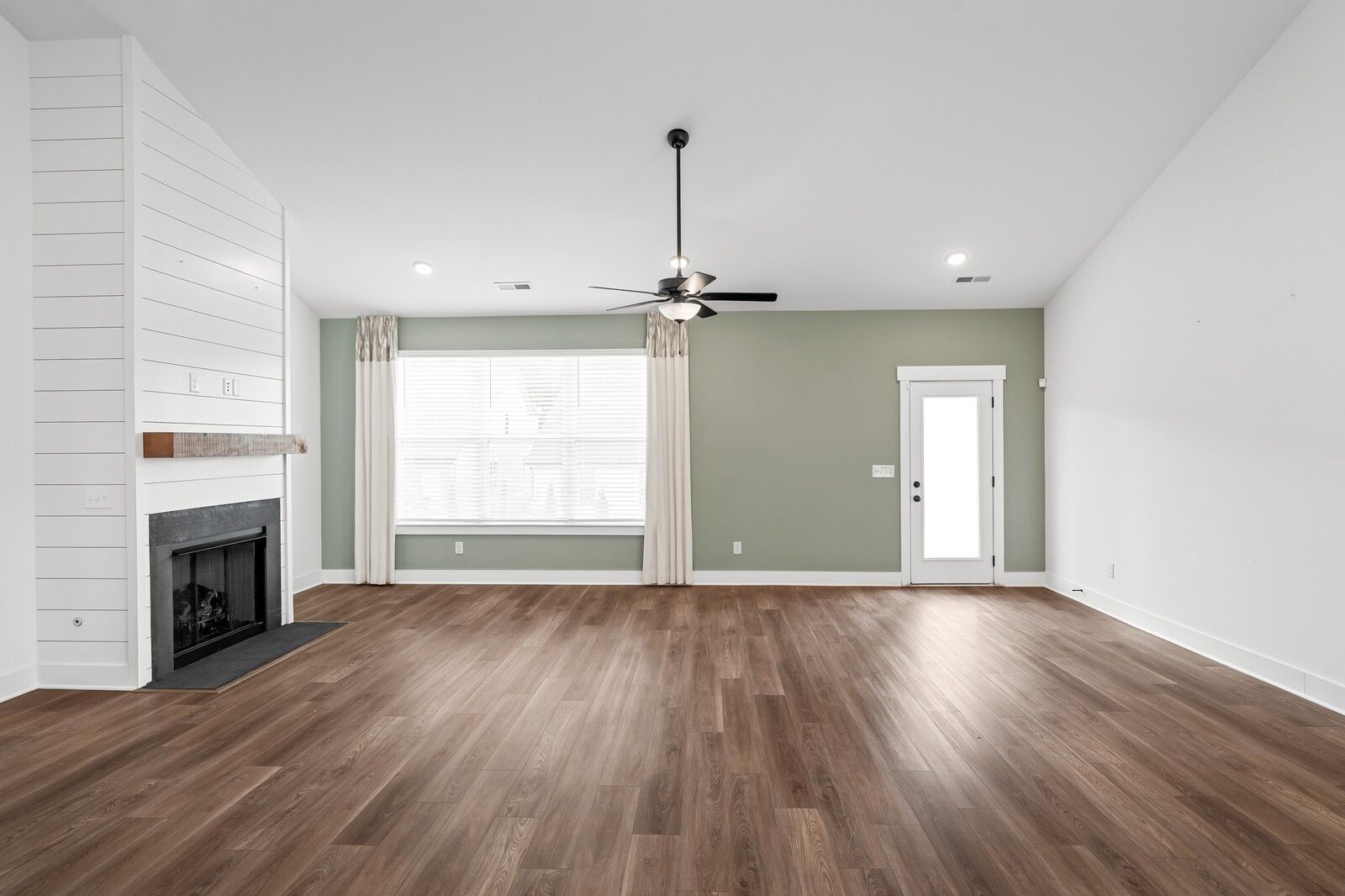 Cozy living room with shiplap fireplace, hardwood floors, and large windows in Davidson Homes Ridgeport, Gallatin, TN