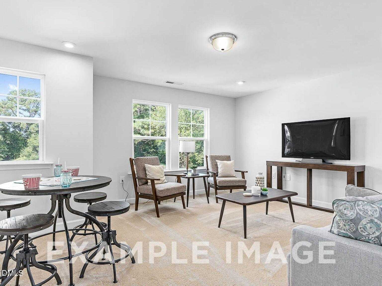 Cozy living room with leather armchairs, round table, flat-screen TV, and large windows in 3-bedroom Davidson Homes The Chestnut B, Lillington, NC